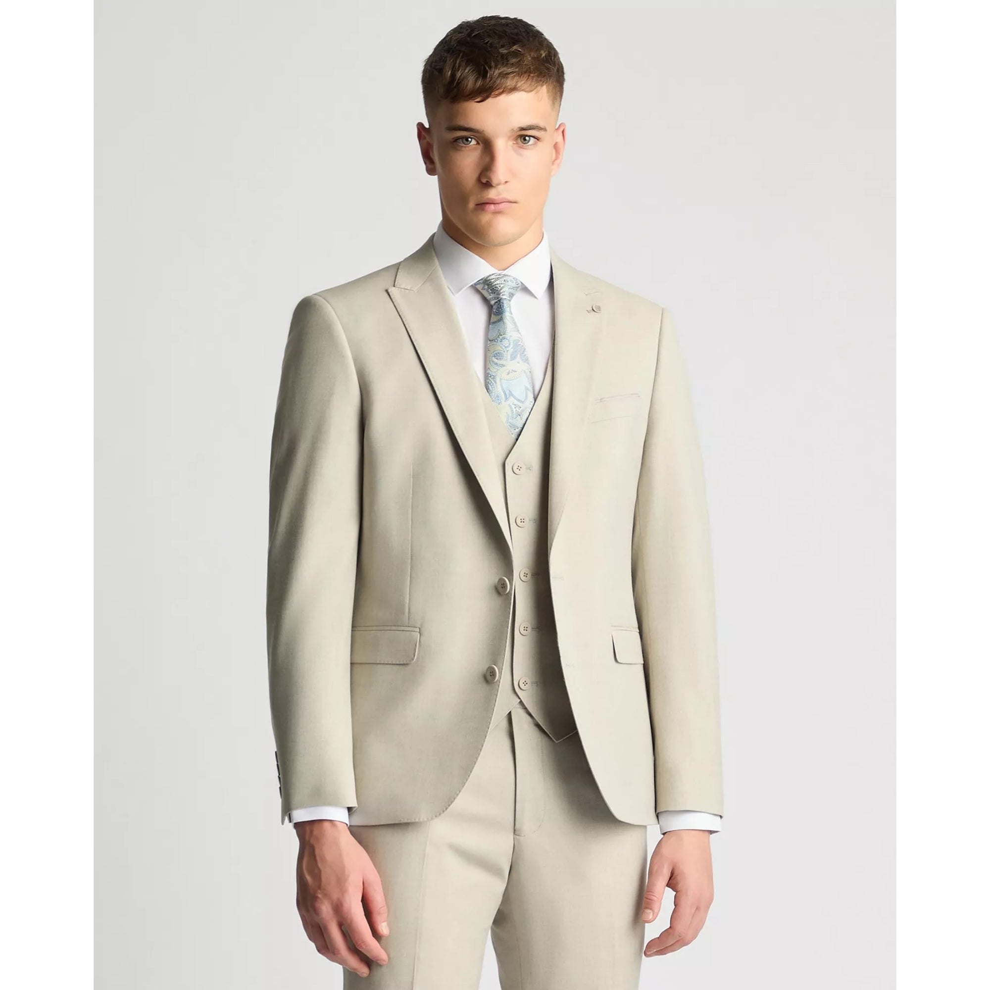 Man wearing a beige suit with a light blue tie on a plain background