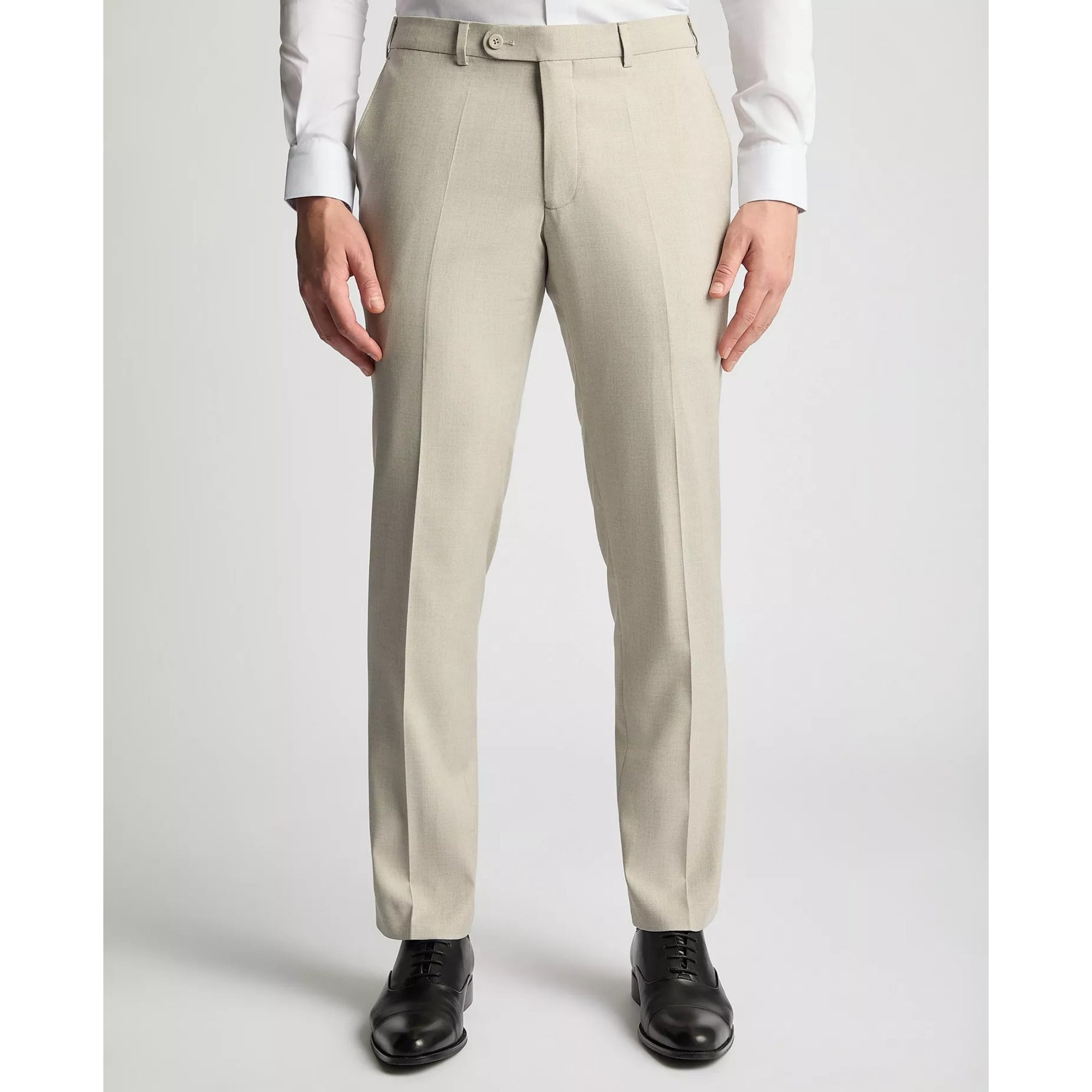 Beige dress pants worn with a white shirt and black shoes on a light gray background