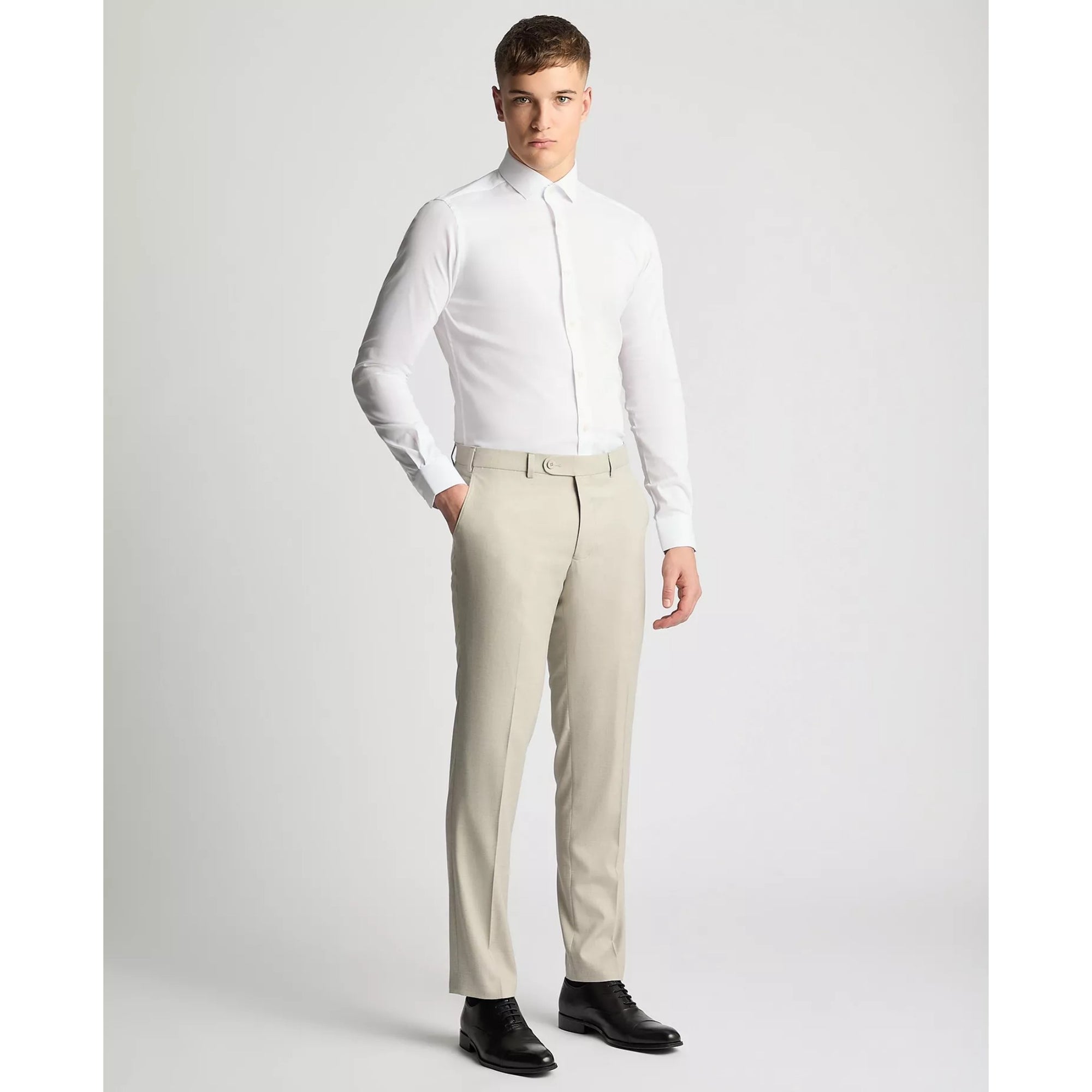 Man wearing a white dress shirt and beige pants on a plain background