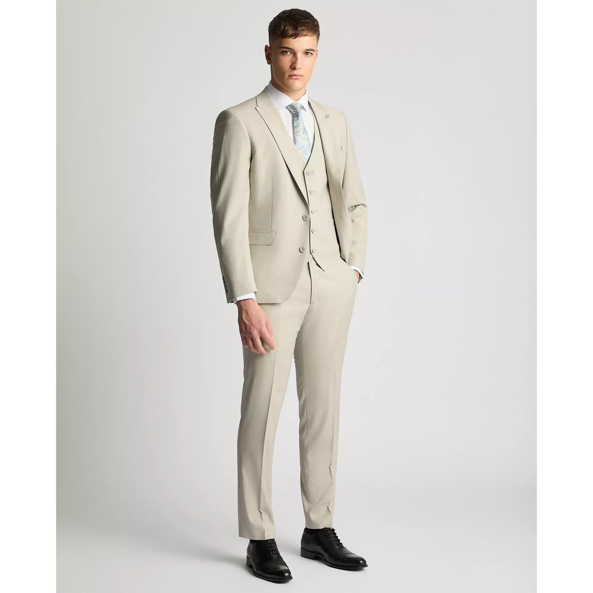 Man wearing a beige suit with a white shirt and black shoes on a light gray background