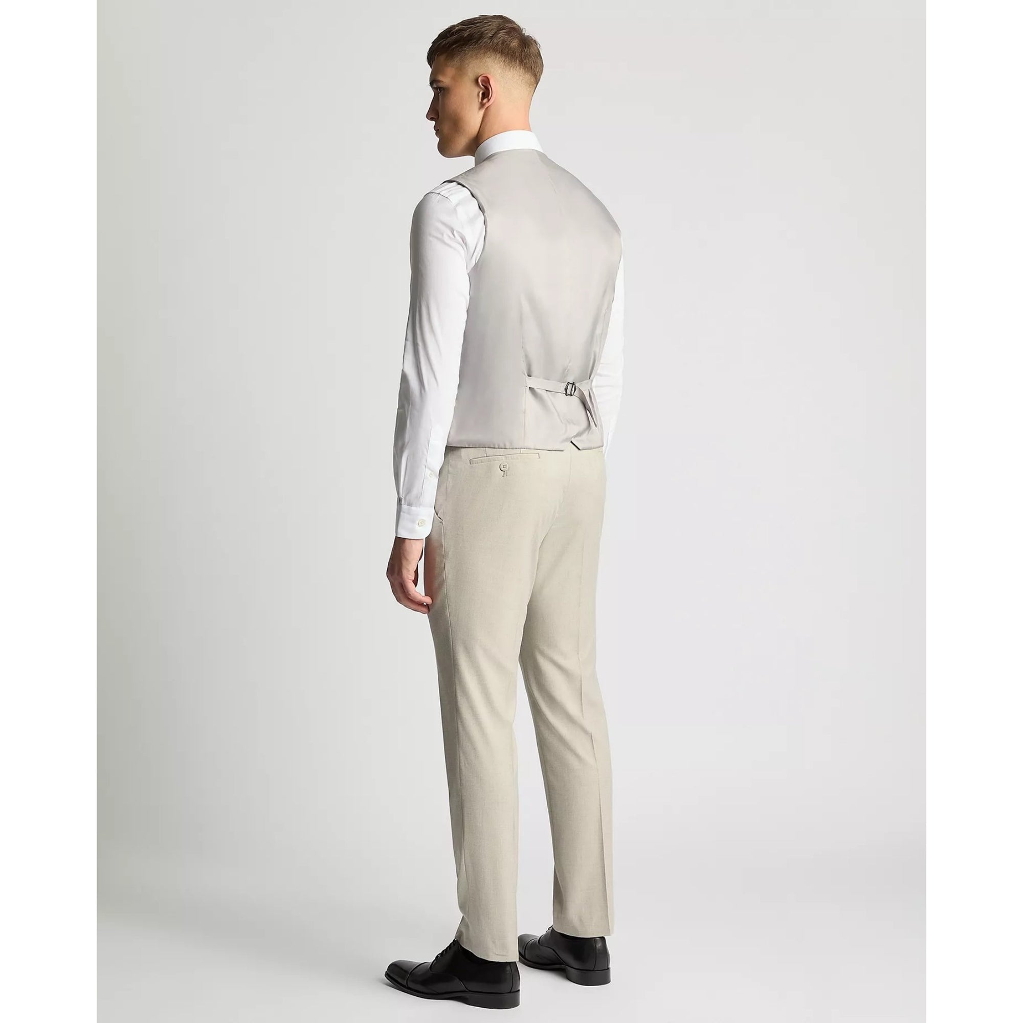 Man wearing a light gray vest and beige pants on a white background