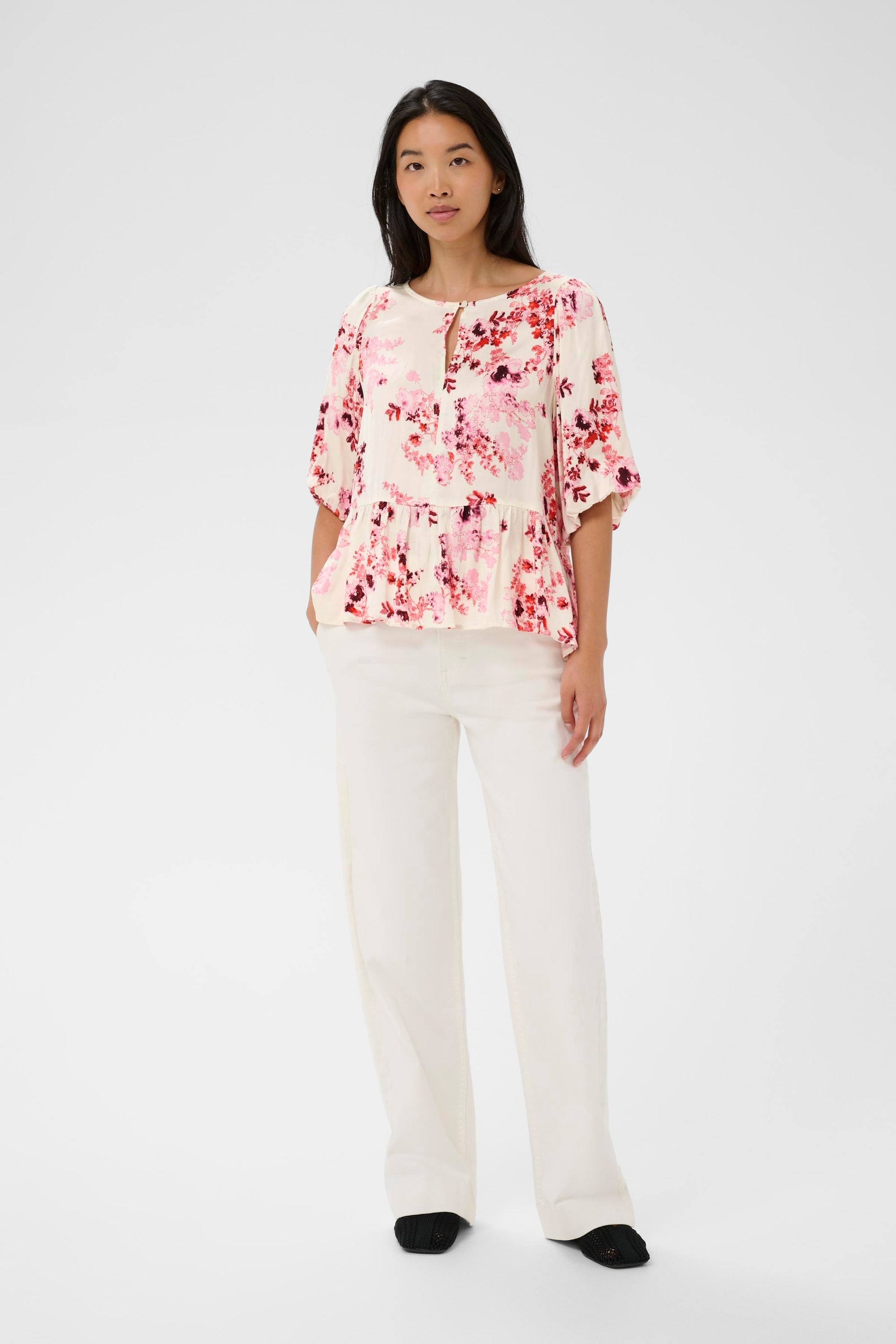 Woman wearing a floral blouse and white pants on a white background