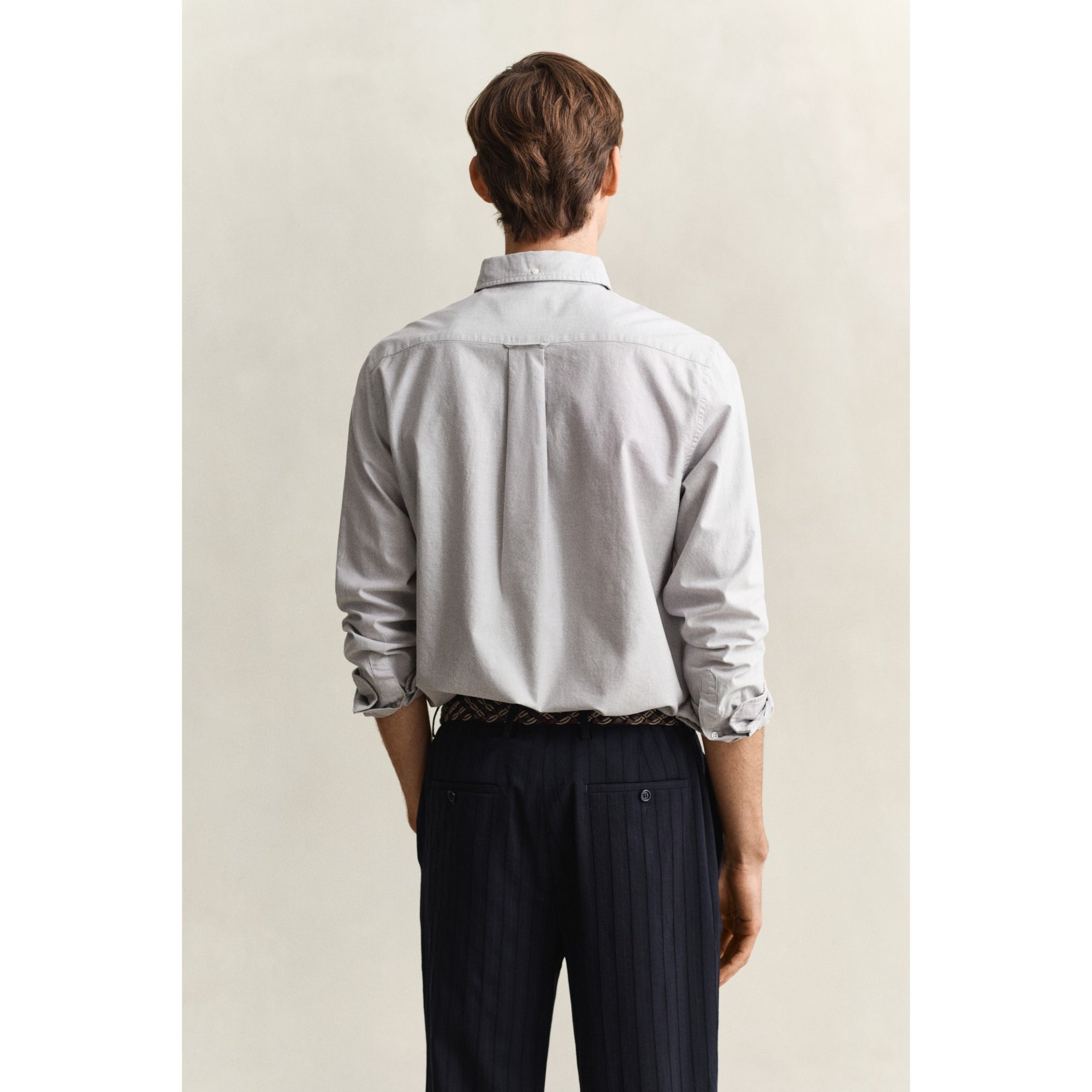 Man wearing a light gray shirt and dark pants against a plain background