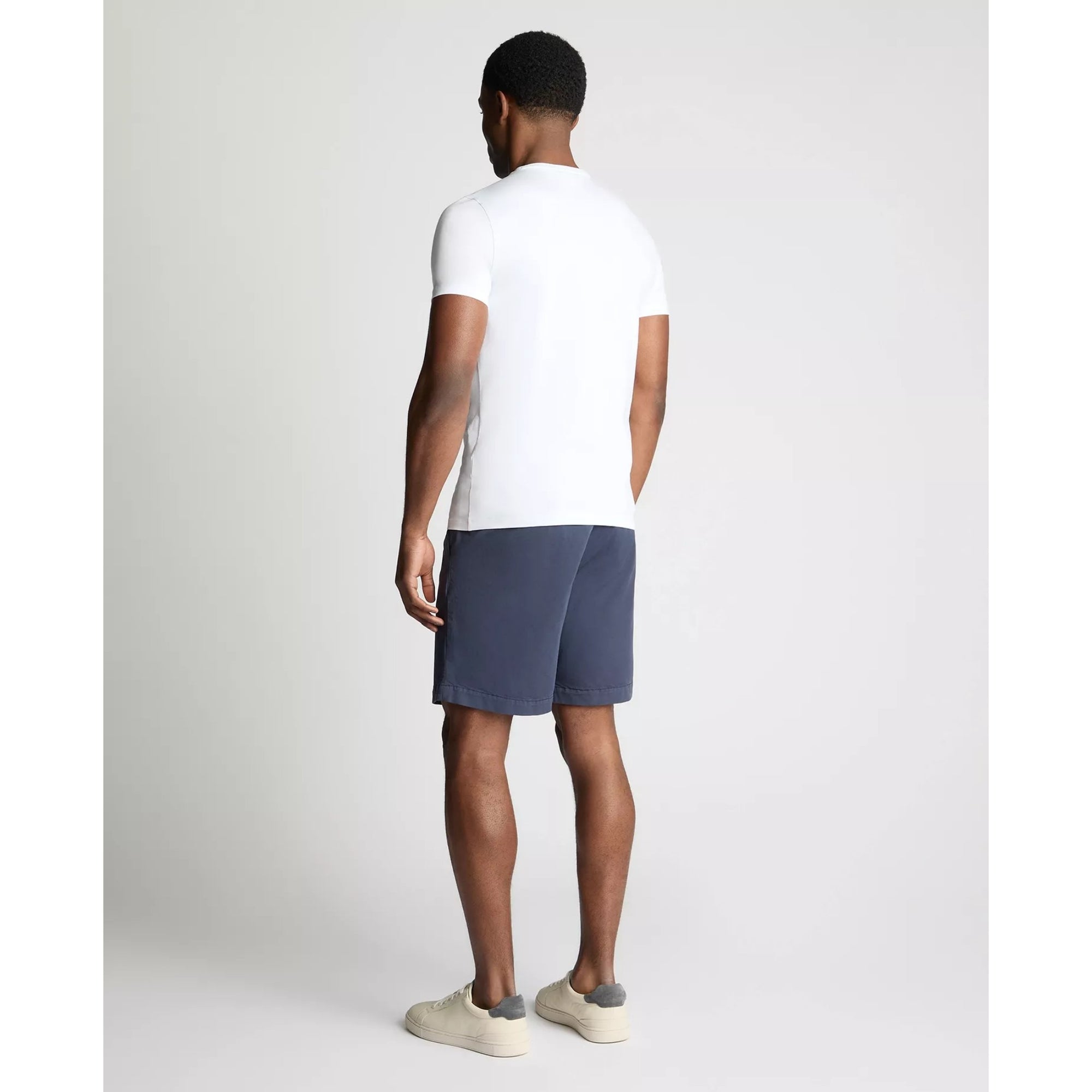 Man wearing a white t-shirt and navy shorts on a plain background