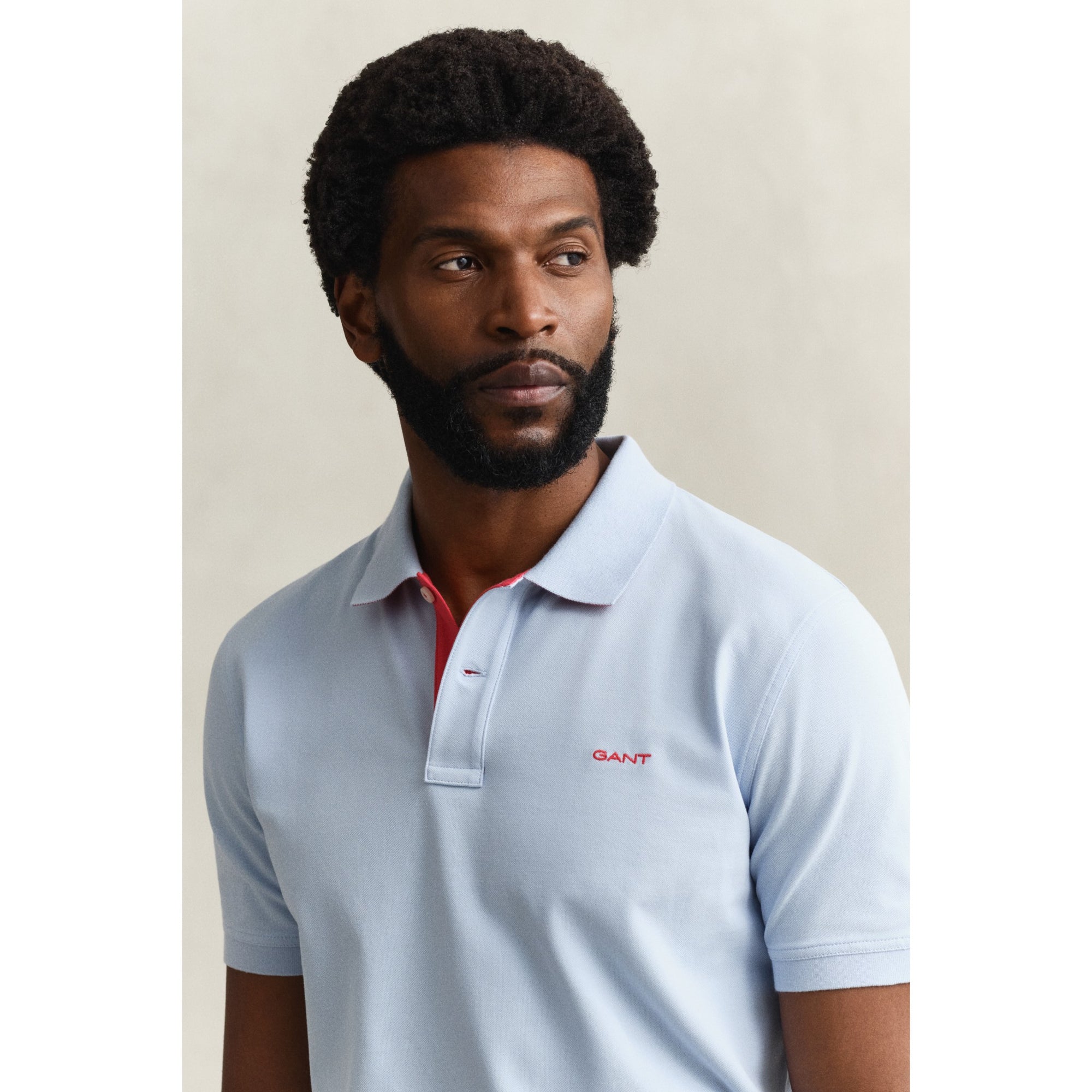 Man wearing a light blue polo shirt with a brand logo on a plain background