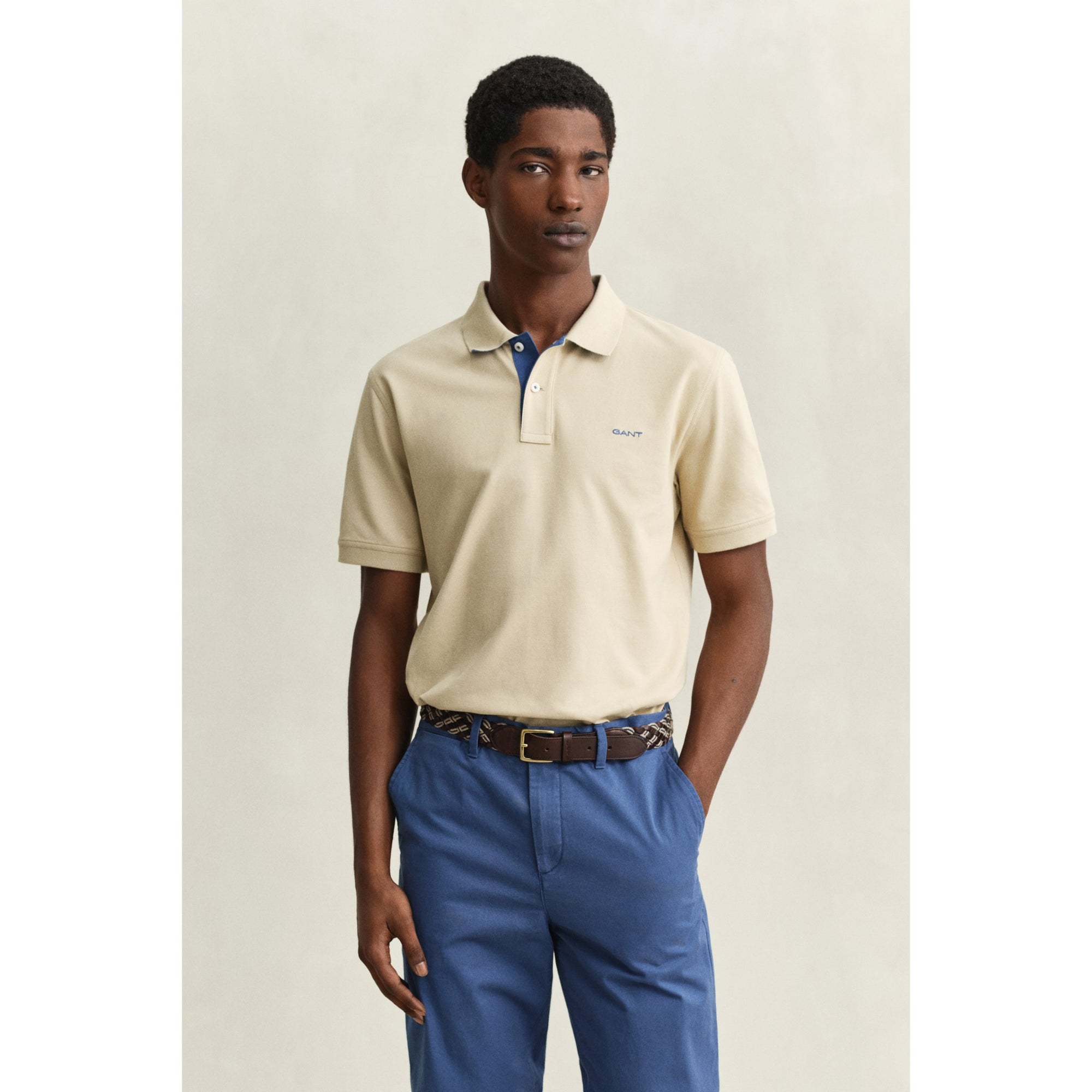 Man wearing a beige polo shirt and blue pants against a neutral background