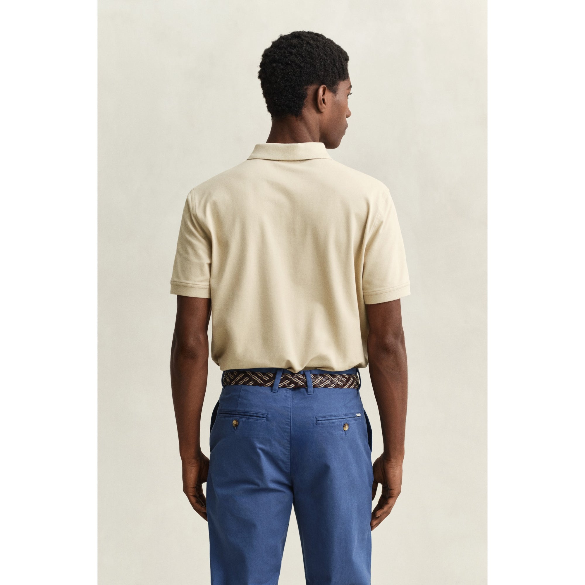 Man wearing a beige polo shirt and blue pants on a plain background