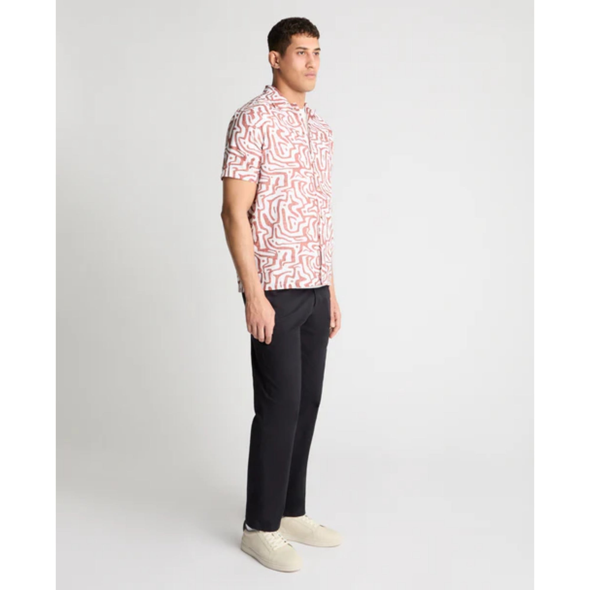 Man wearing a patterned shirt and black pants on a white background