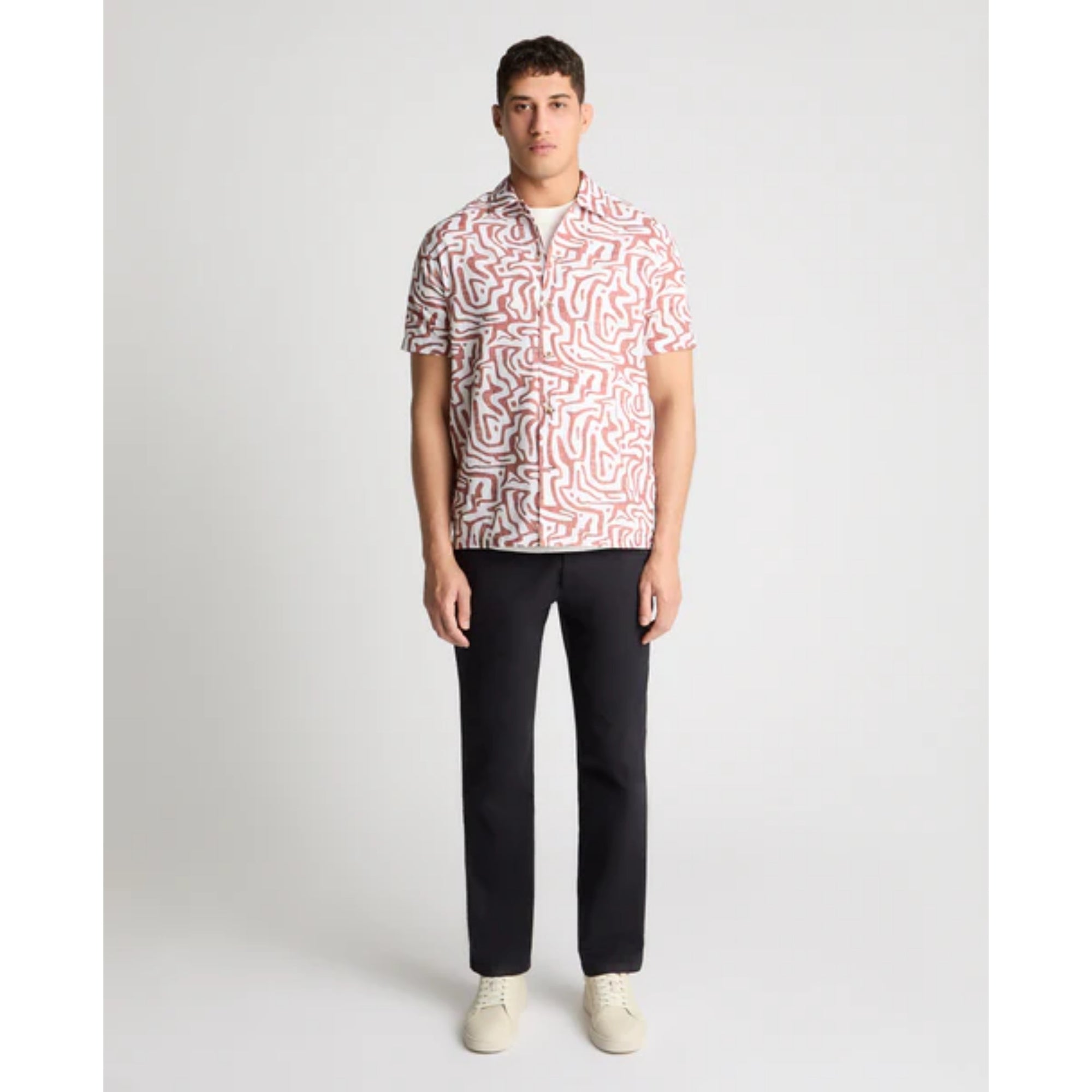 Man wearing a patterned shirt and black pants on a white background