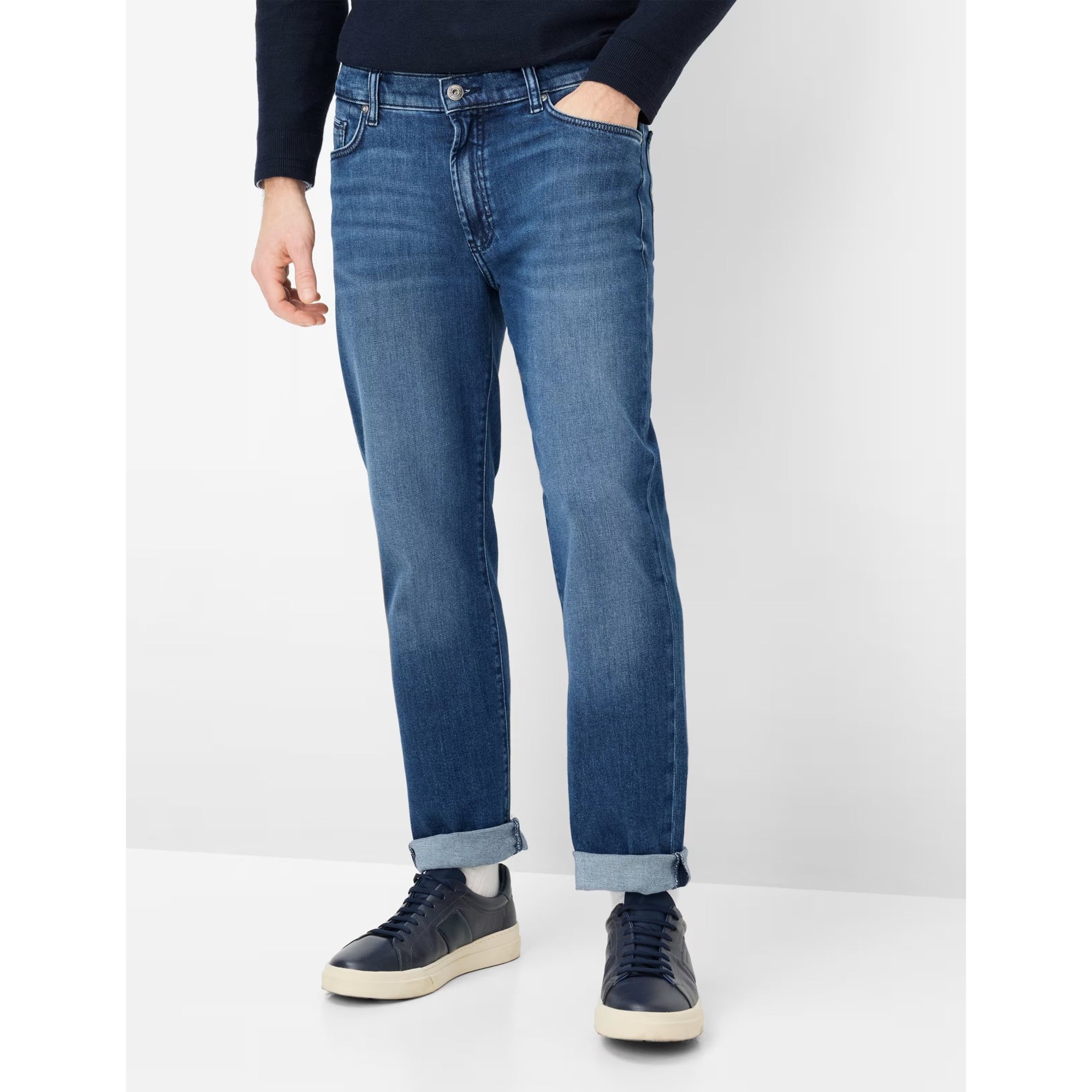 Person wearing blue jeans and dark shoes on a white background
