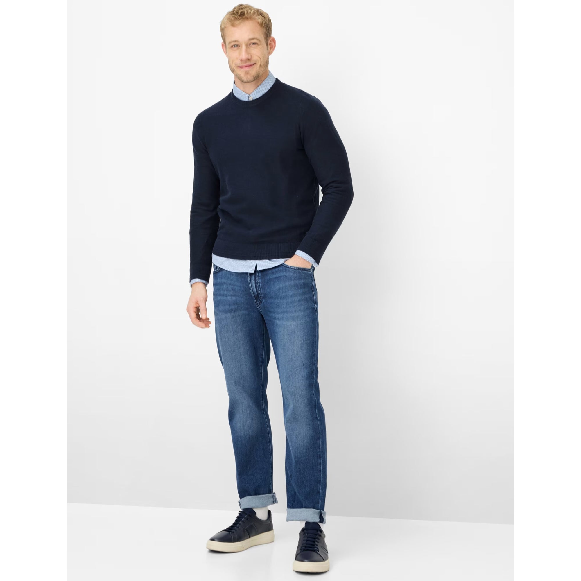 Man wearing a navy sweater and blue jeans on a white background