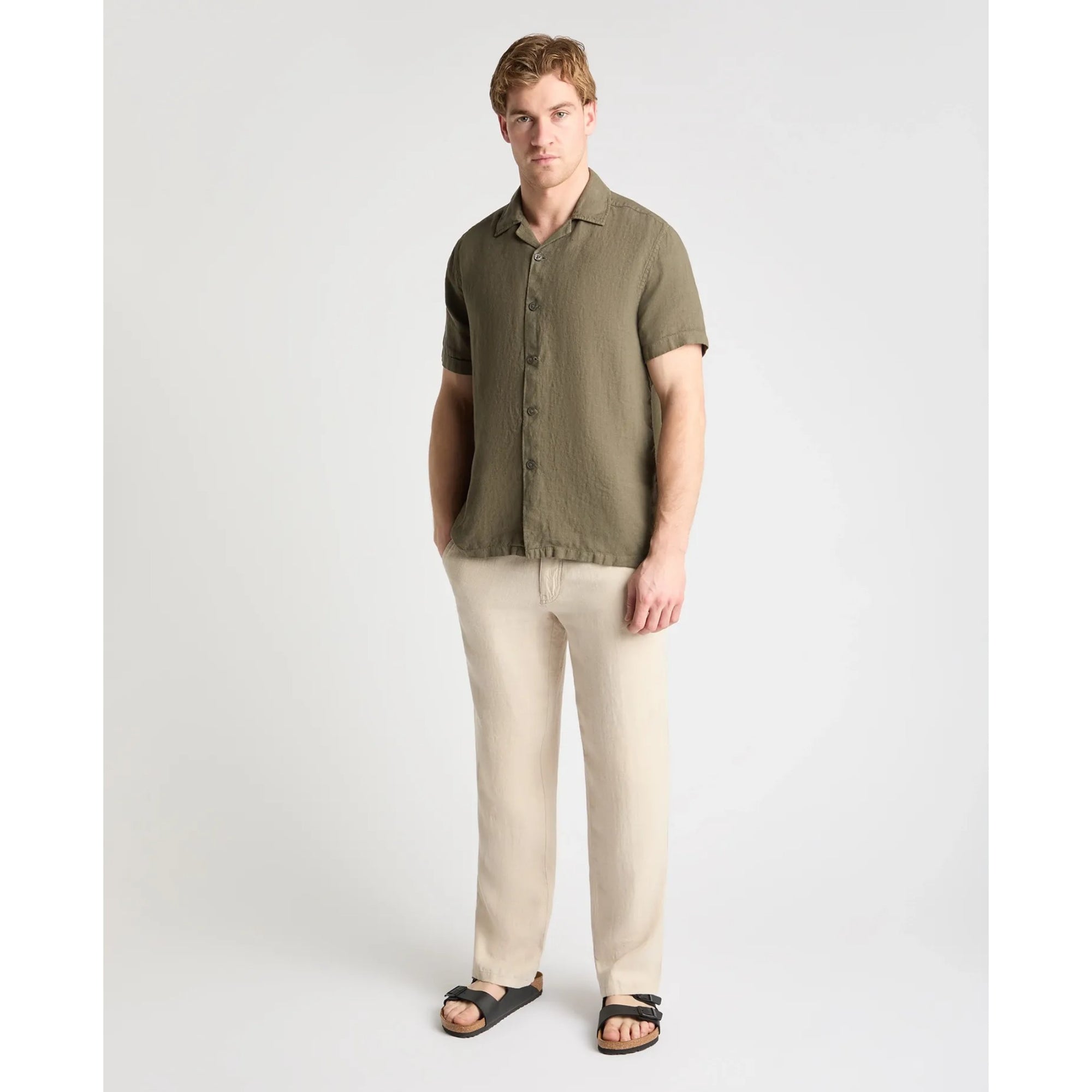 Man wearing an olive green shirt and beige pants on a white background