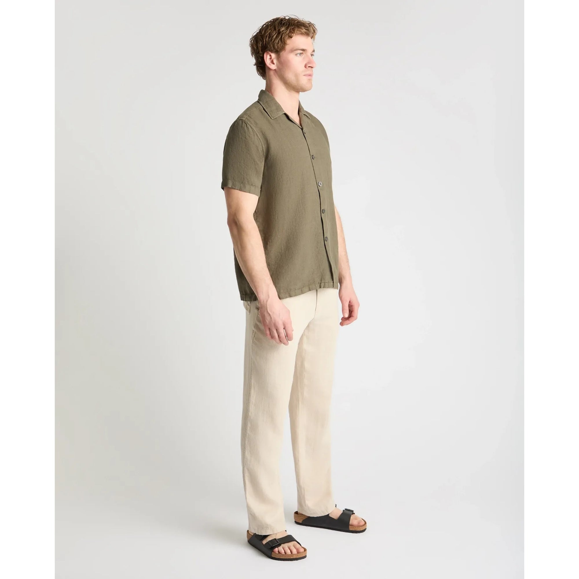 Man wearing an olive green shirt and beige pants on a white background