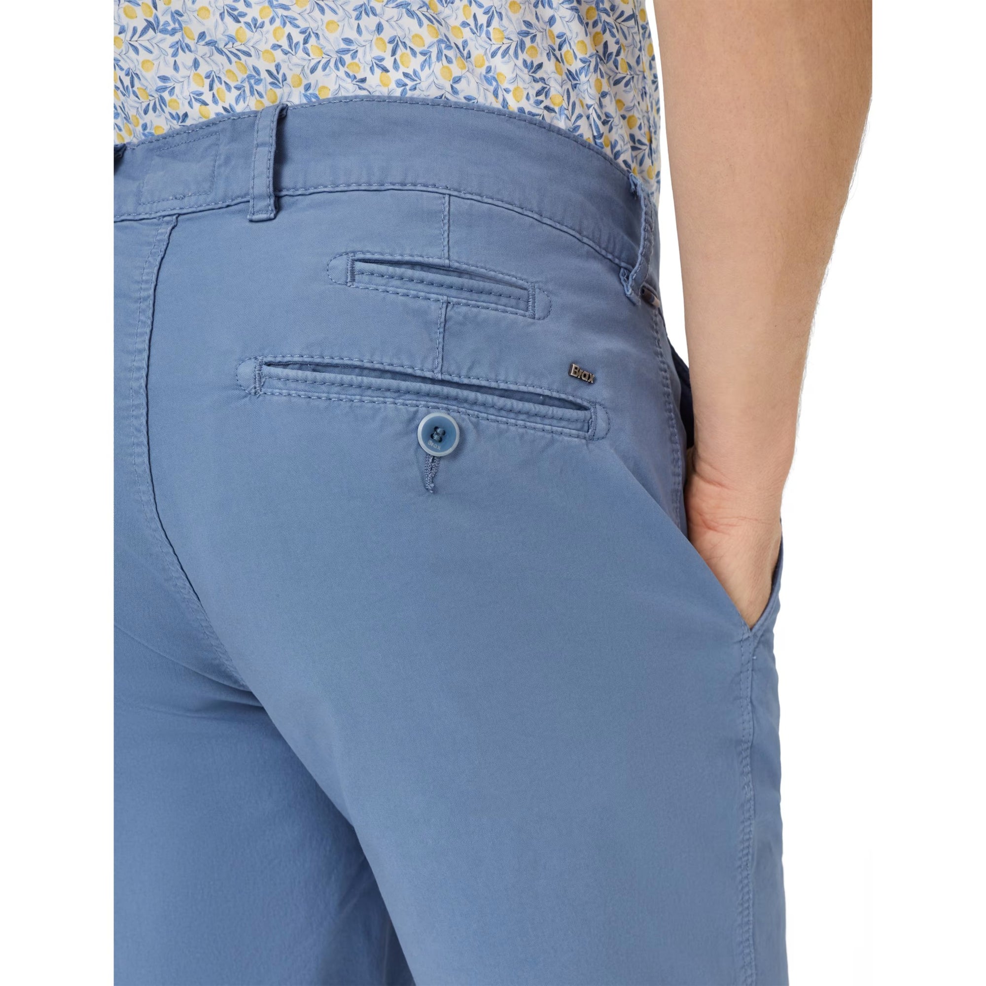 Blue pants with a floral shirt worn underneath on a white background