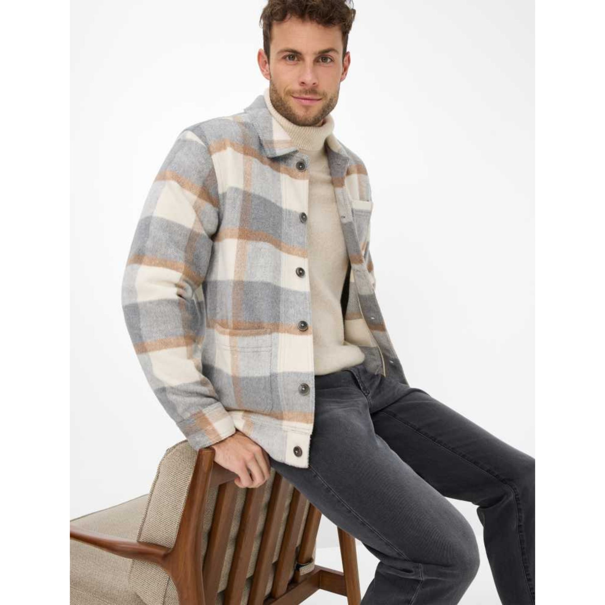 Man wearing a plaid shirt over a turtleneck sweater with dark pants on a white background