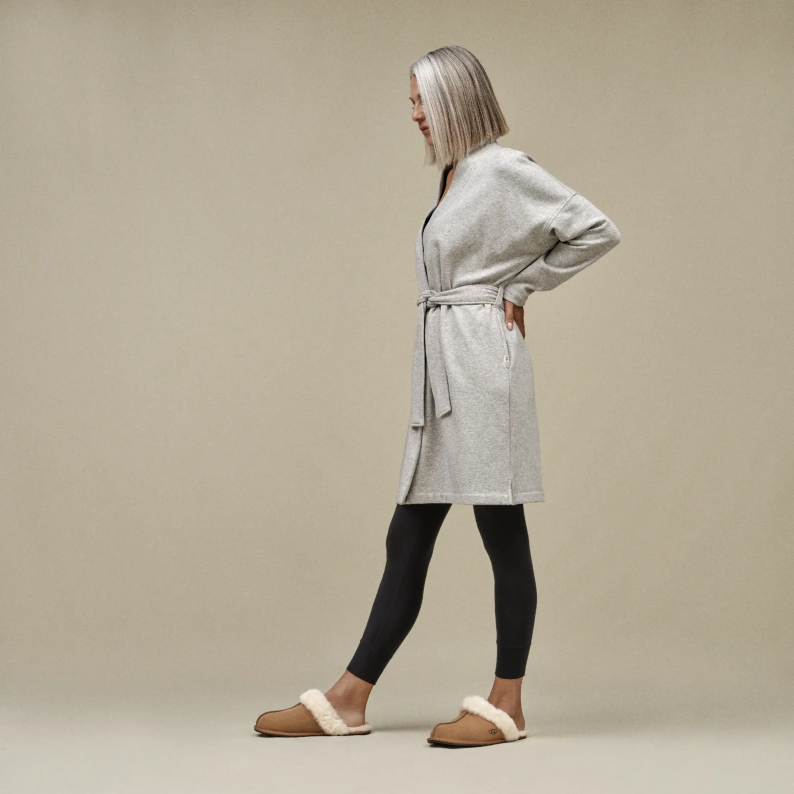 Woman wearing a gray robe and black leggings on a beige background