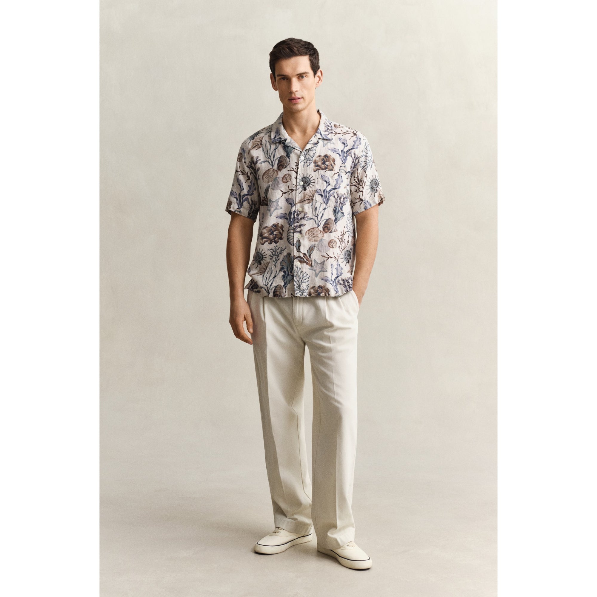 Man wearing a floral shirt and white pants against a plain background
