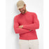 A man wearing a red crew neck jumper with long sleeves, paired with light-colored trousers and a beige cap.