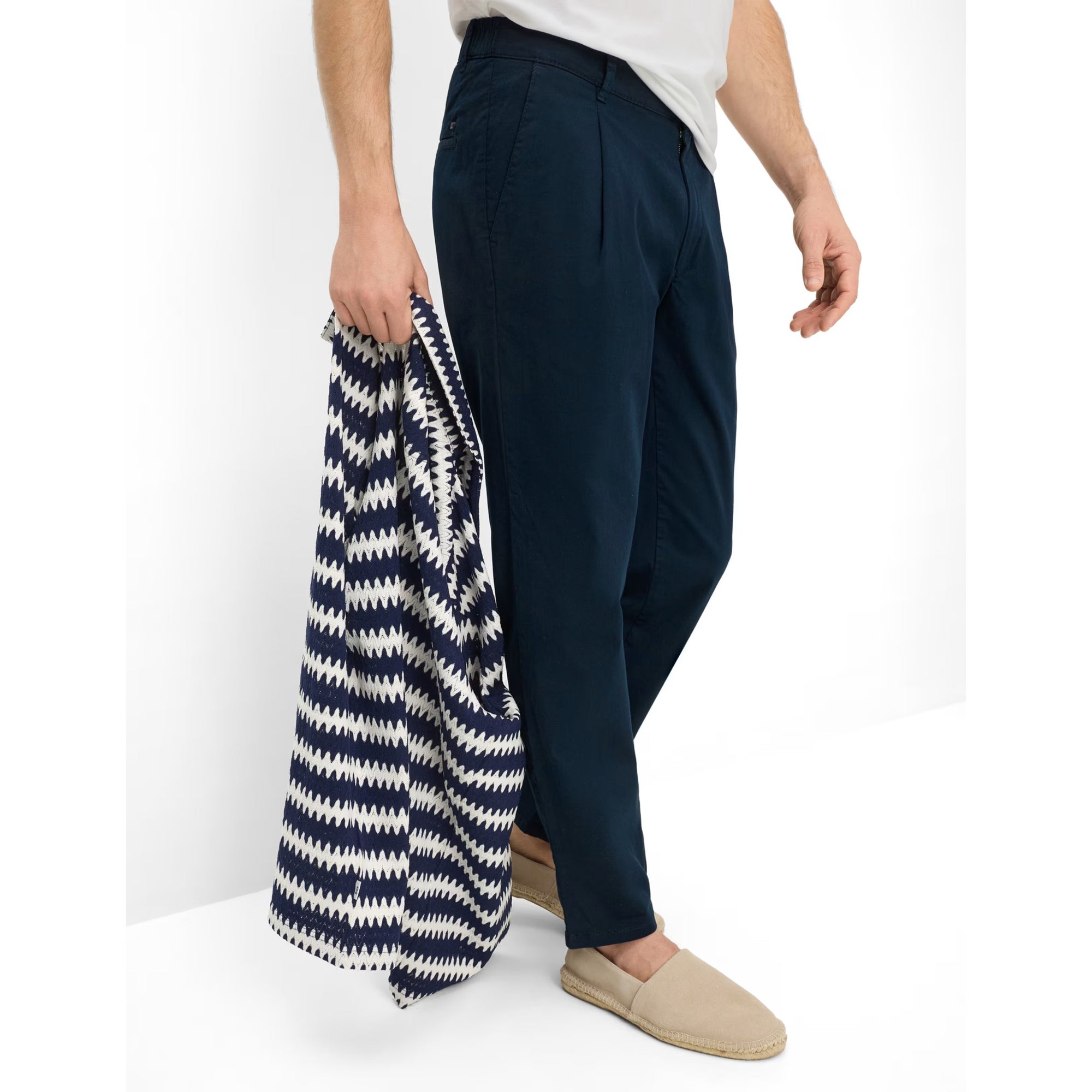 Person holding a navy and white patterned bag with dark blue pants and beige shoes on a white background