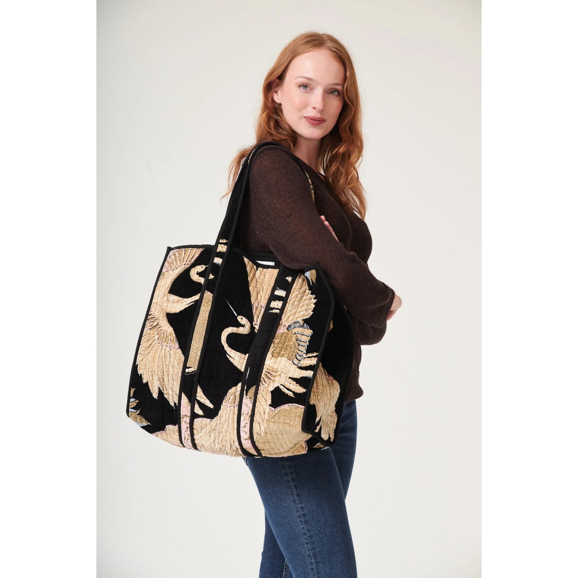 Woman holding a large black and beige patterned bag against a white background