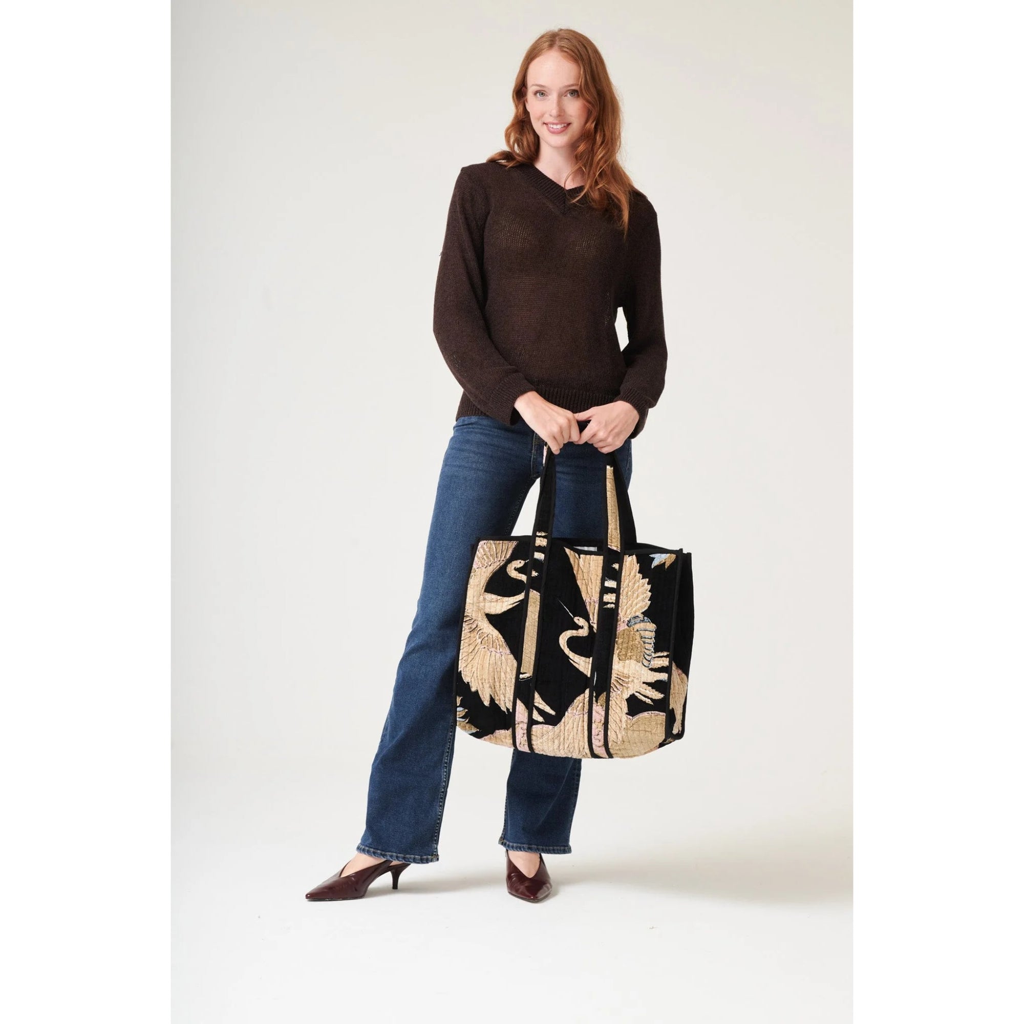 Woman holding a black and beige tote bag against a white background