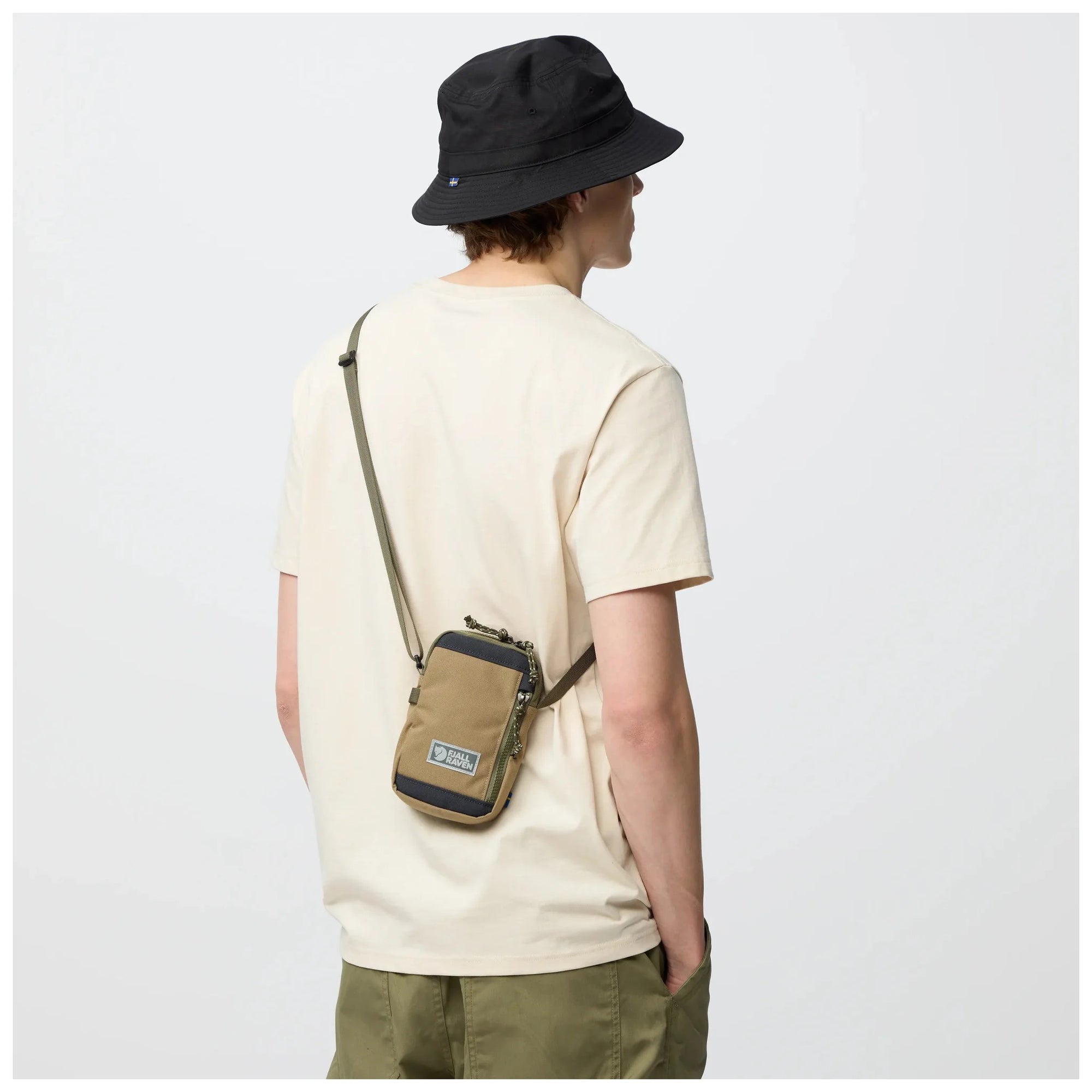 Person wearing a beige crossbody bag and black bucket hat on a white background