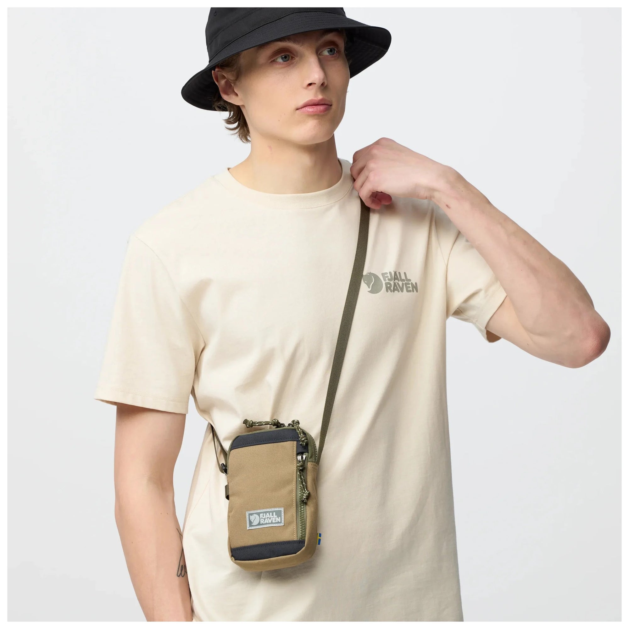 Person wearing a beige t-shirt with a small bag over their shoulder on a light gray background