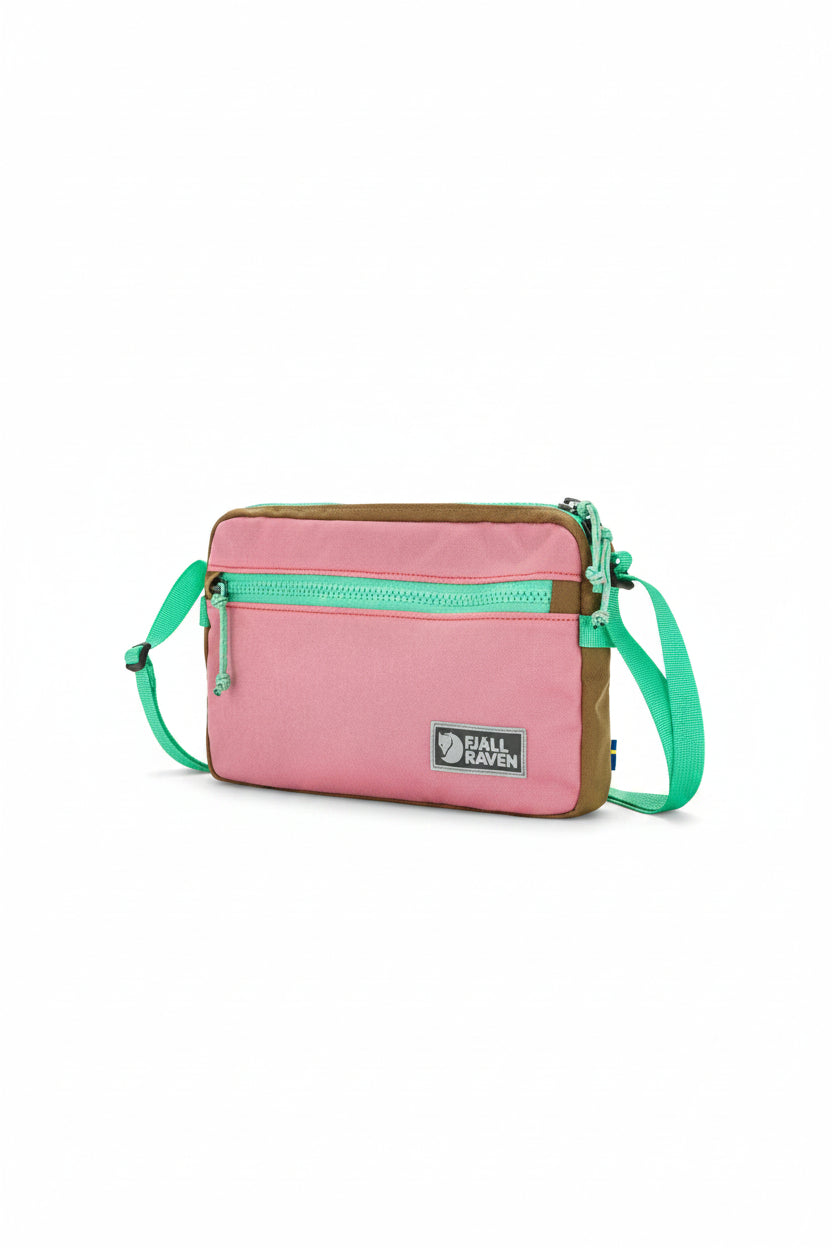 Pink crossbody bag with green strap and brown accents on a white background