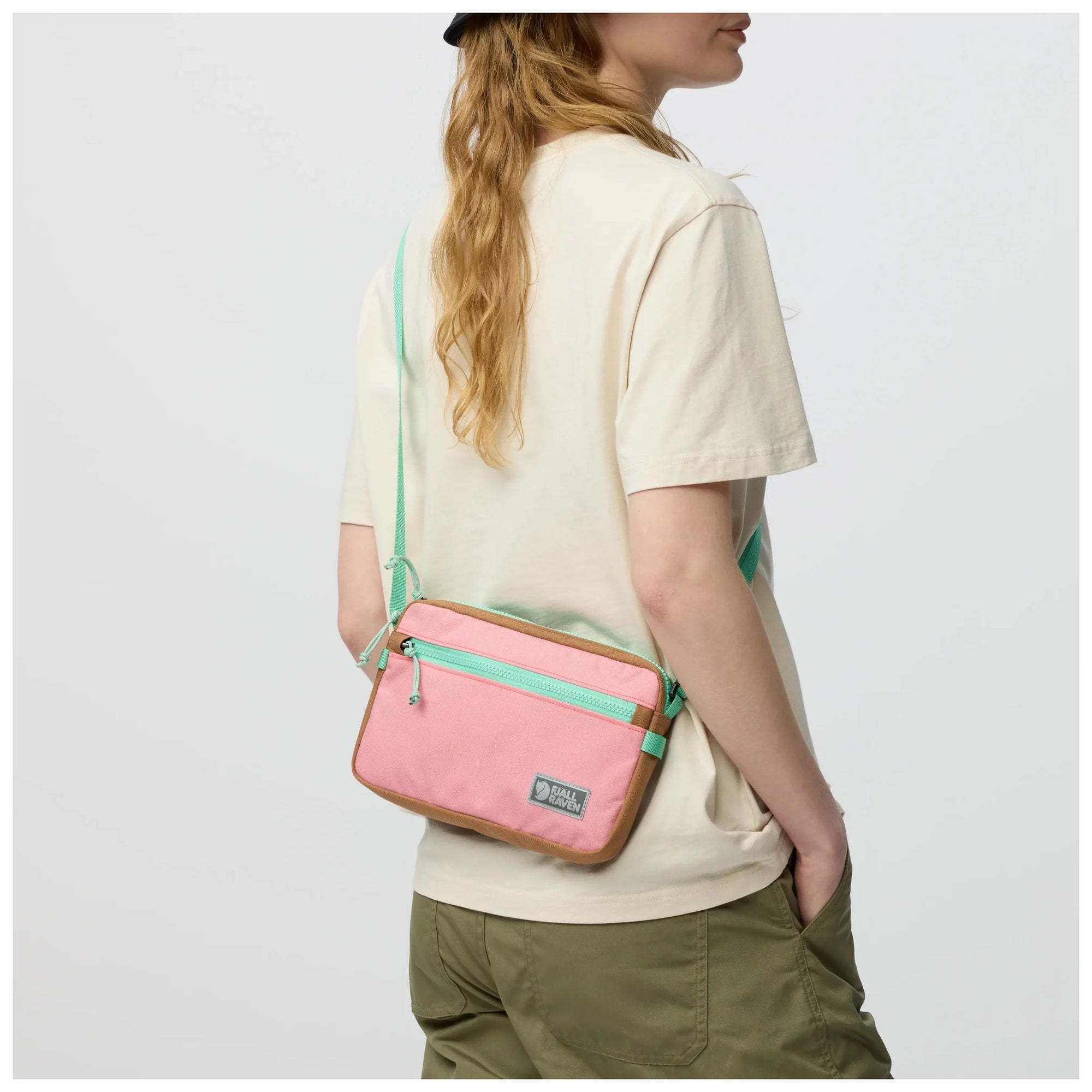 Person wearing a pink crossbody bag with green accents on a white background
