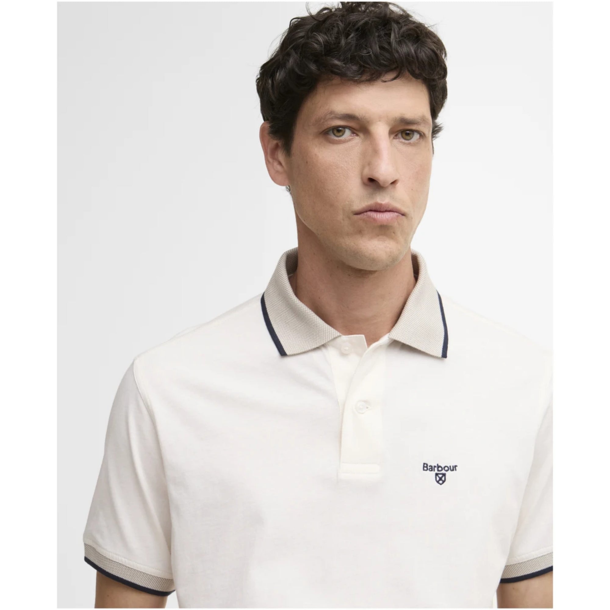 Man wearing a white polo shirt with a brand logo on a light gray background