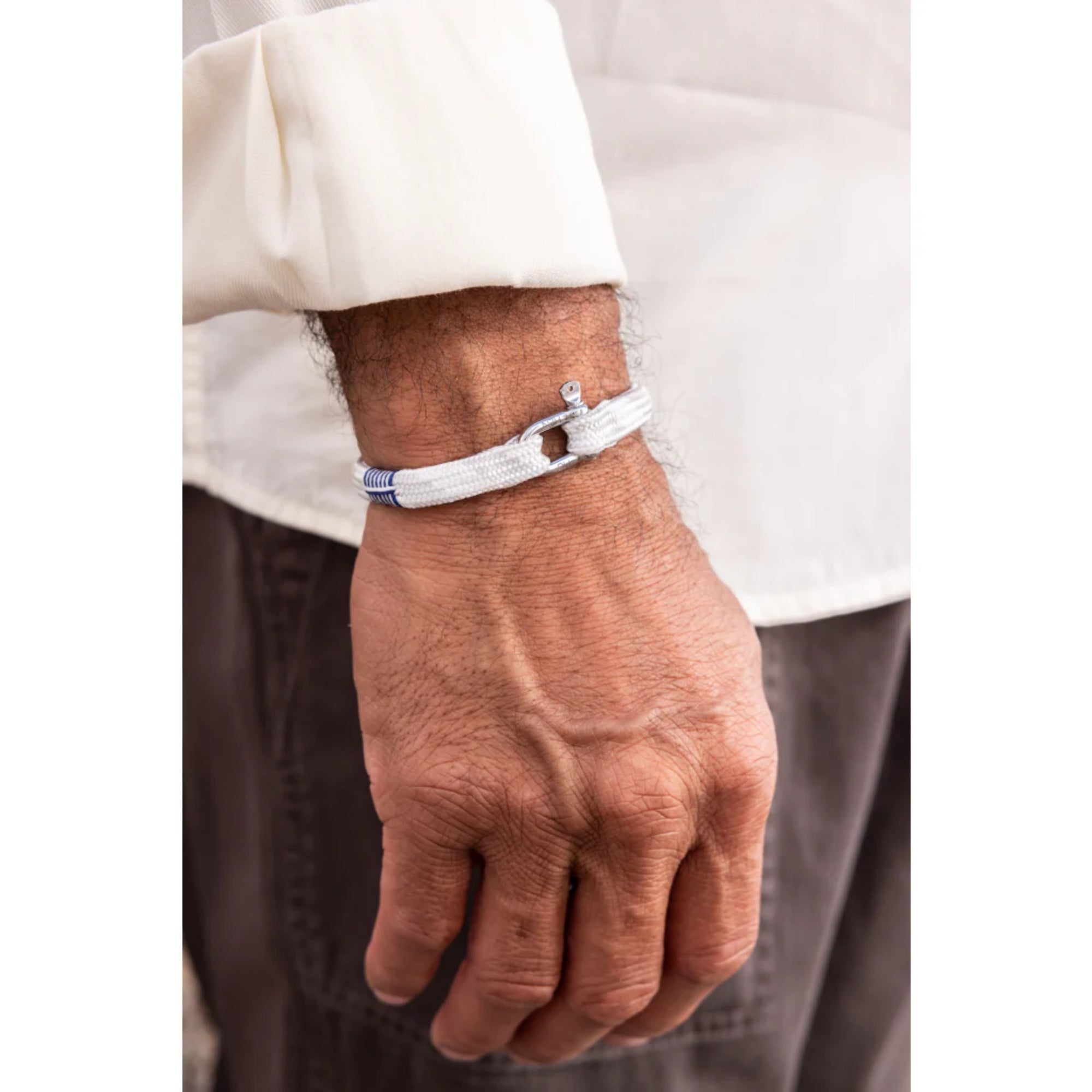 Close-up of a hand wearing a white bracelet with a small charm on a plain background