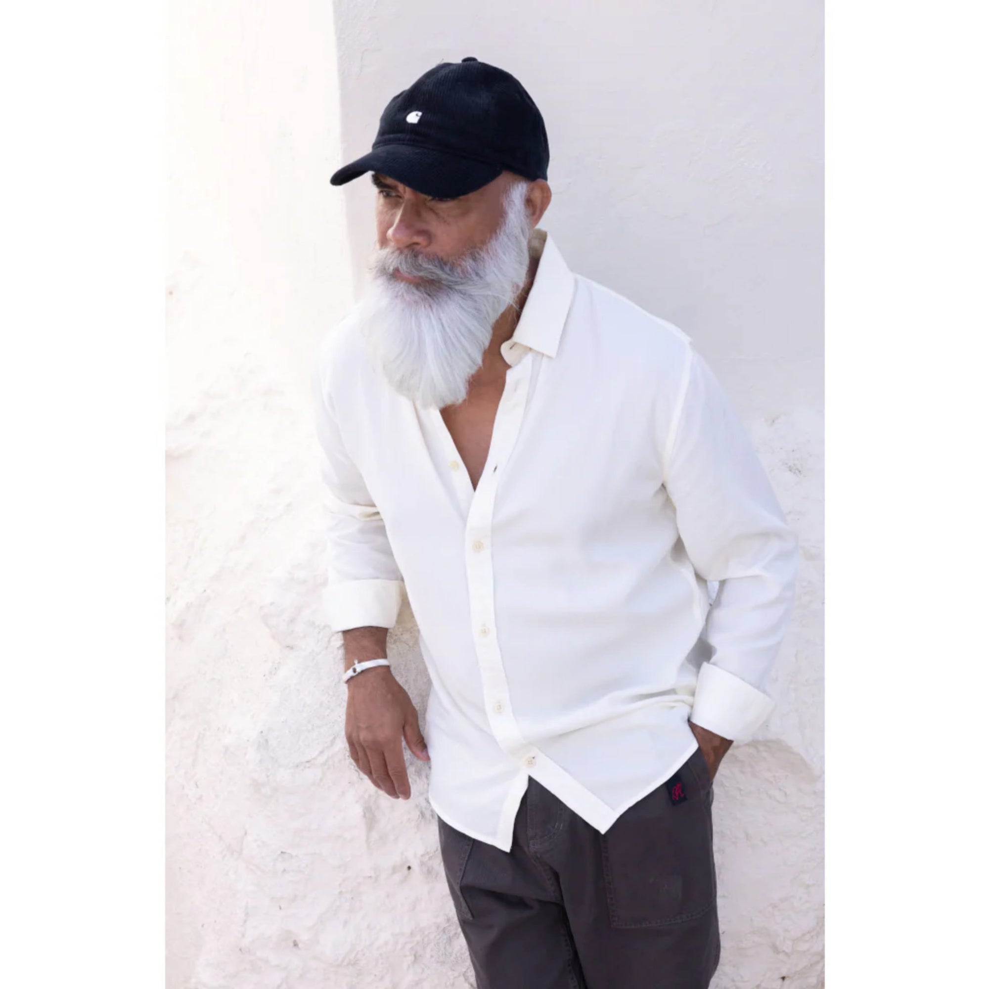 Man wearing a white shirt, dark pants, and a black cap against a light background