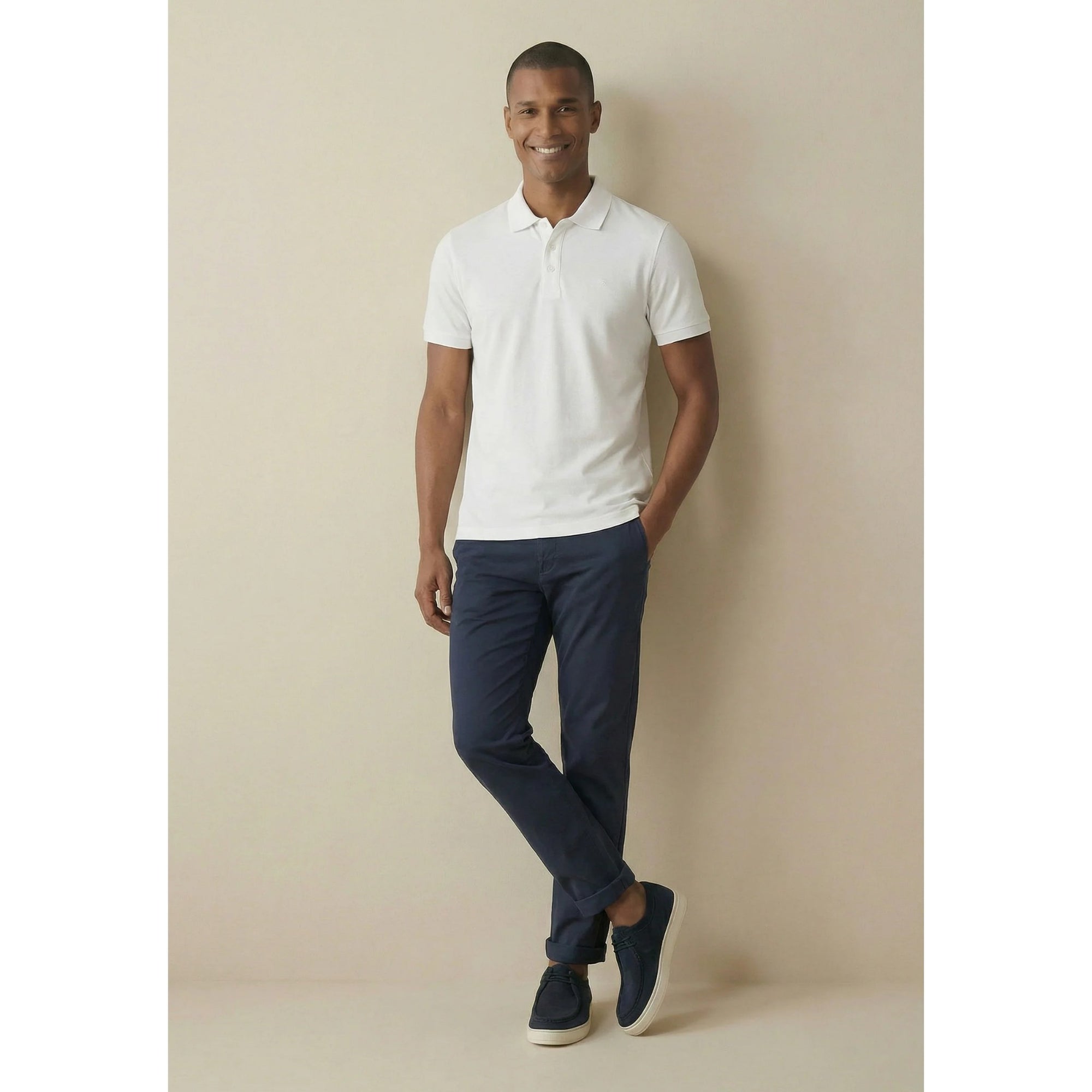 Man wearing a white polo shirt and navy pants against a beige background