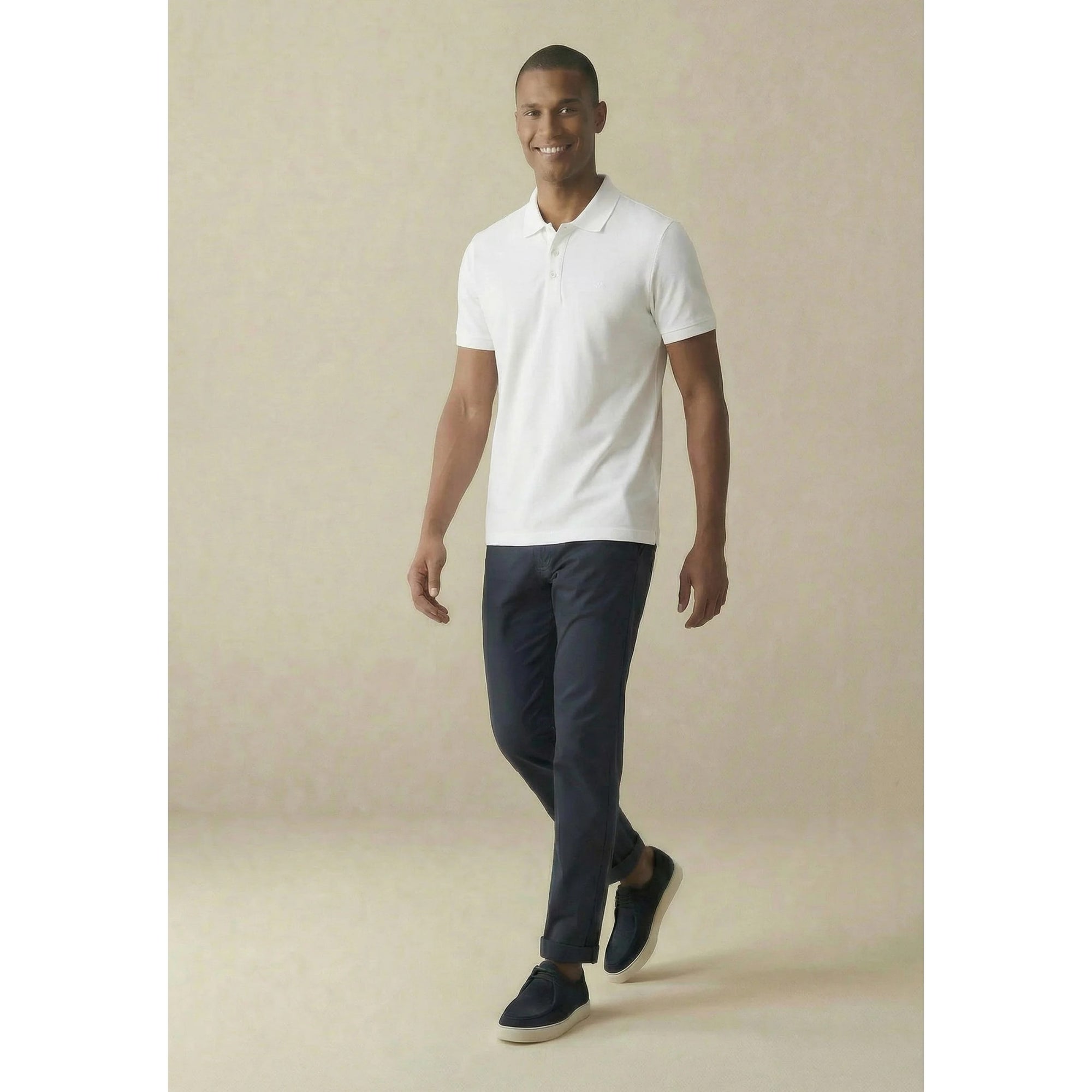 Man wearing a white polo shirt and dark pants against a beige background