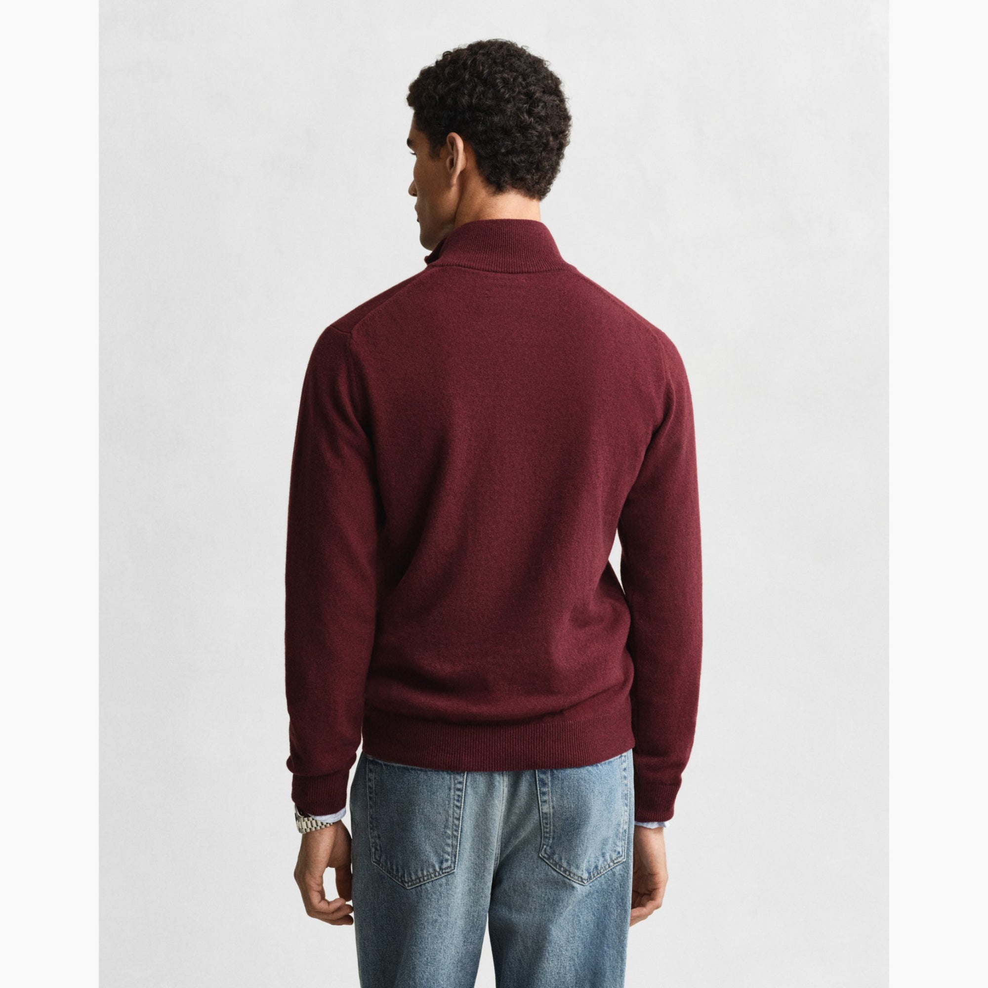 Person wearing a GANT burgundy sweater and light blue jeans on a white background