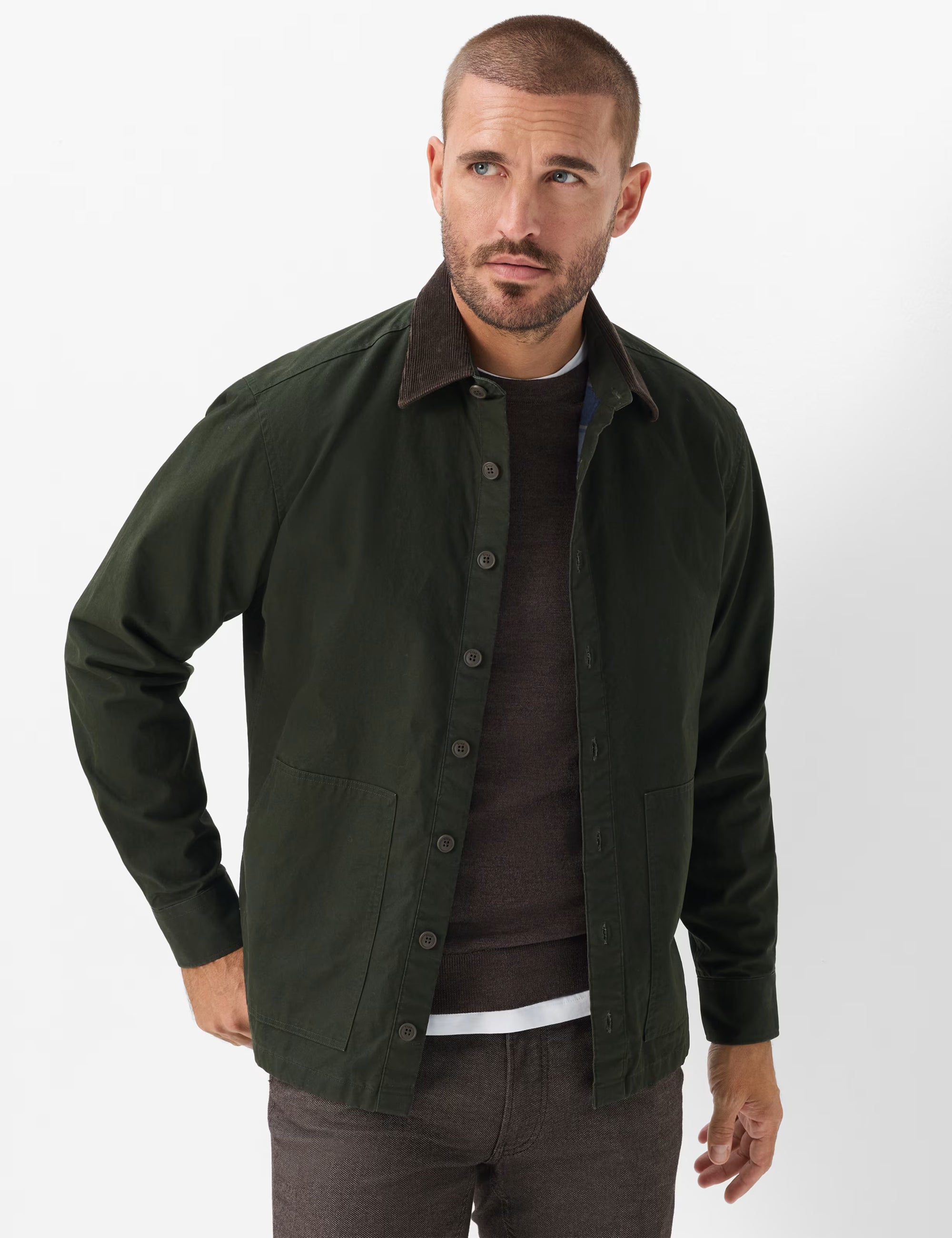 A man wearing an Brax pine green button-up overshirt jacket over a dark brown sweater and dark trousers, photographed against a clean white studio background.