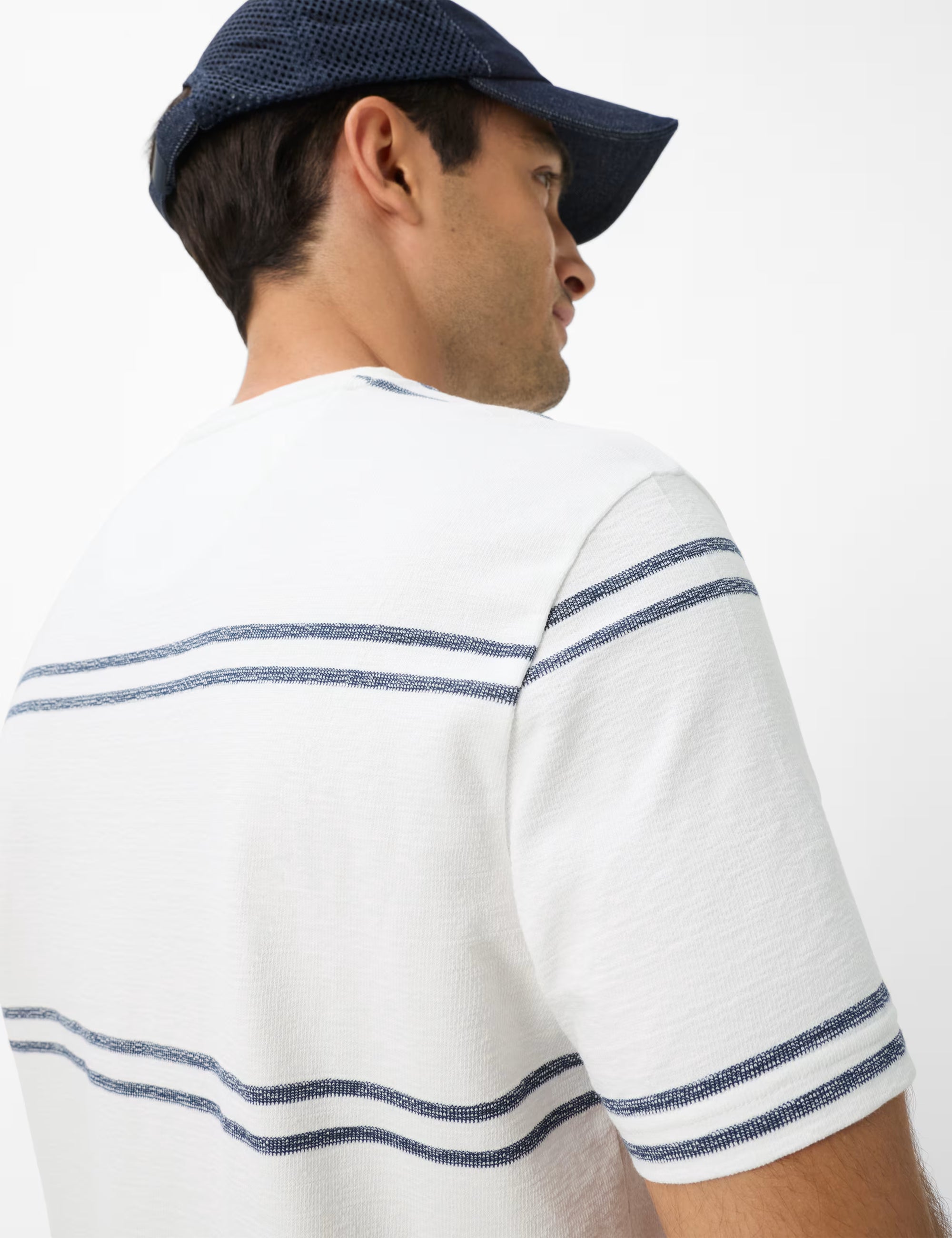 Man wearing a white shirt with blue stripes and a navy cap on a white background
