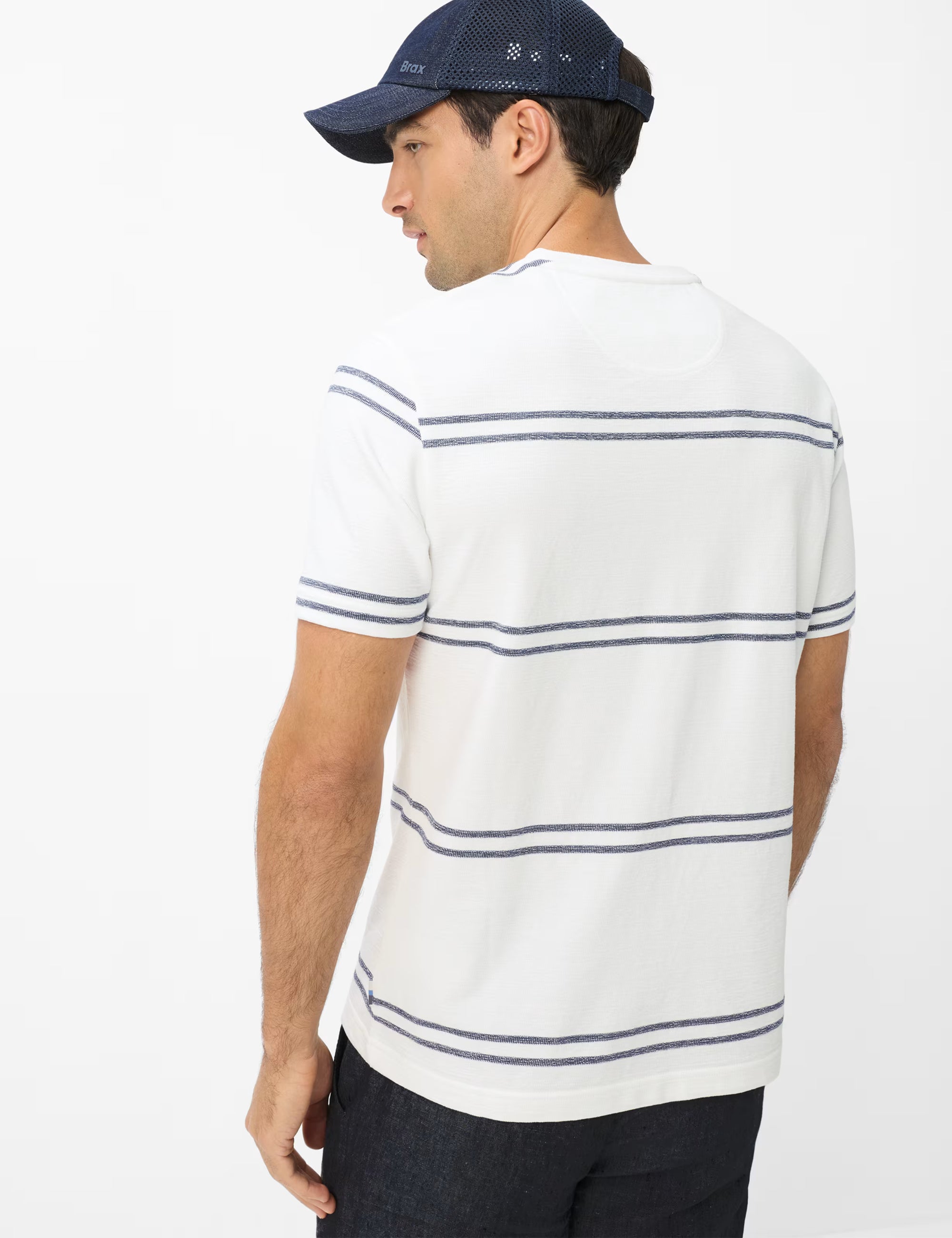 Man wearing a white polo shirt with blue stripes and a navy cap on a white background