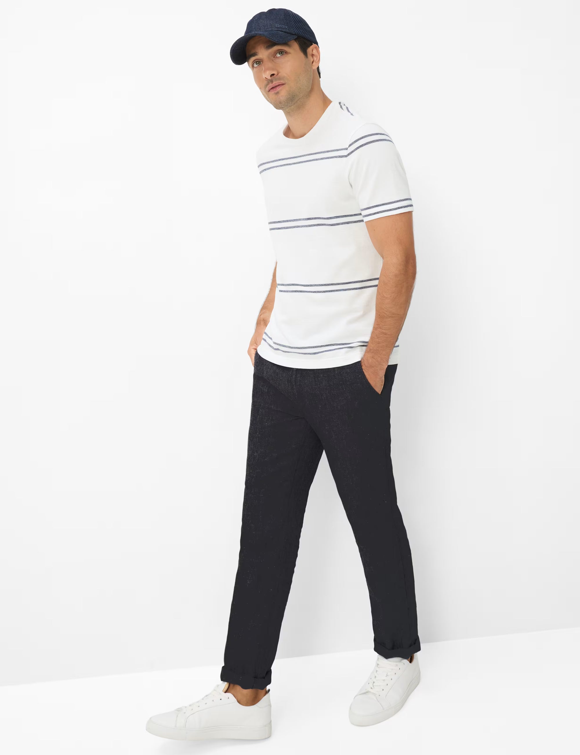 Man wearing a striped shirt, black pants, and a cap against a white background