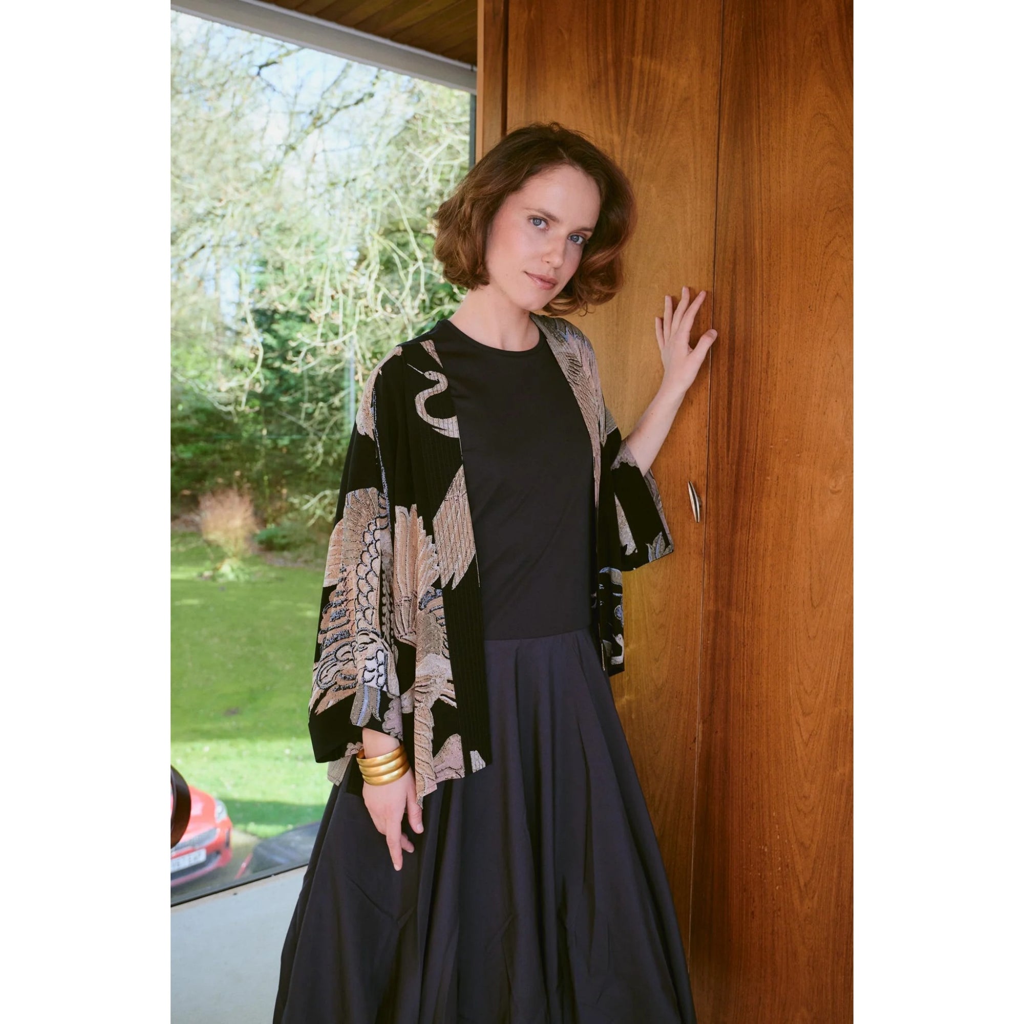 Woman standing indoors by a wooden door with a garden view outside