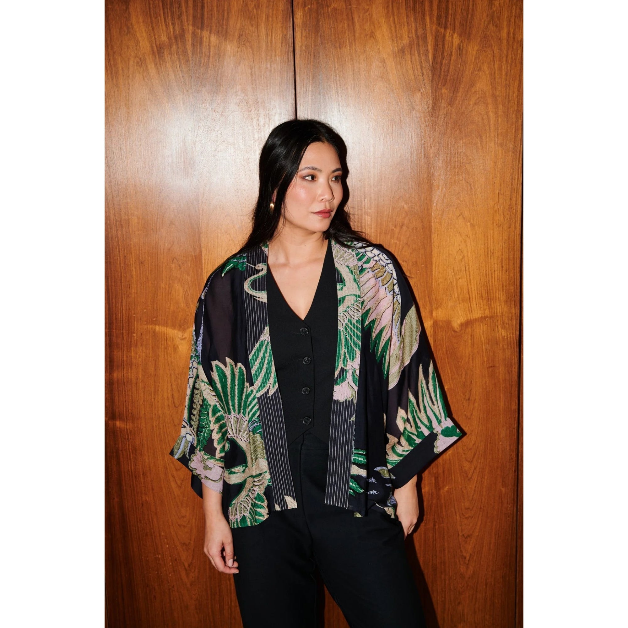 Woman wearing a floral kimono-style jacket against a wooden wall