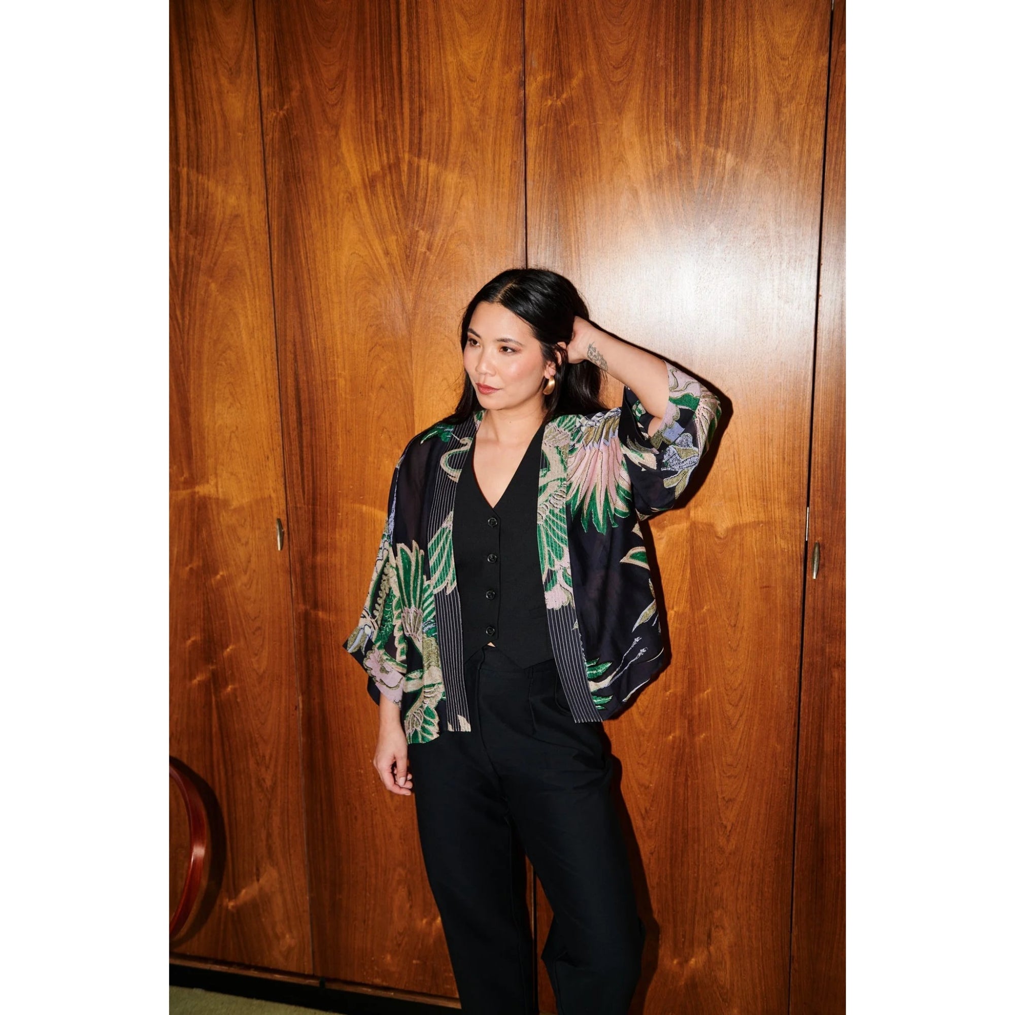 Woman wearing a floral kimono-style jacket against a wooden wall