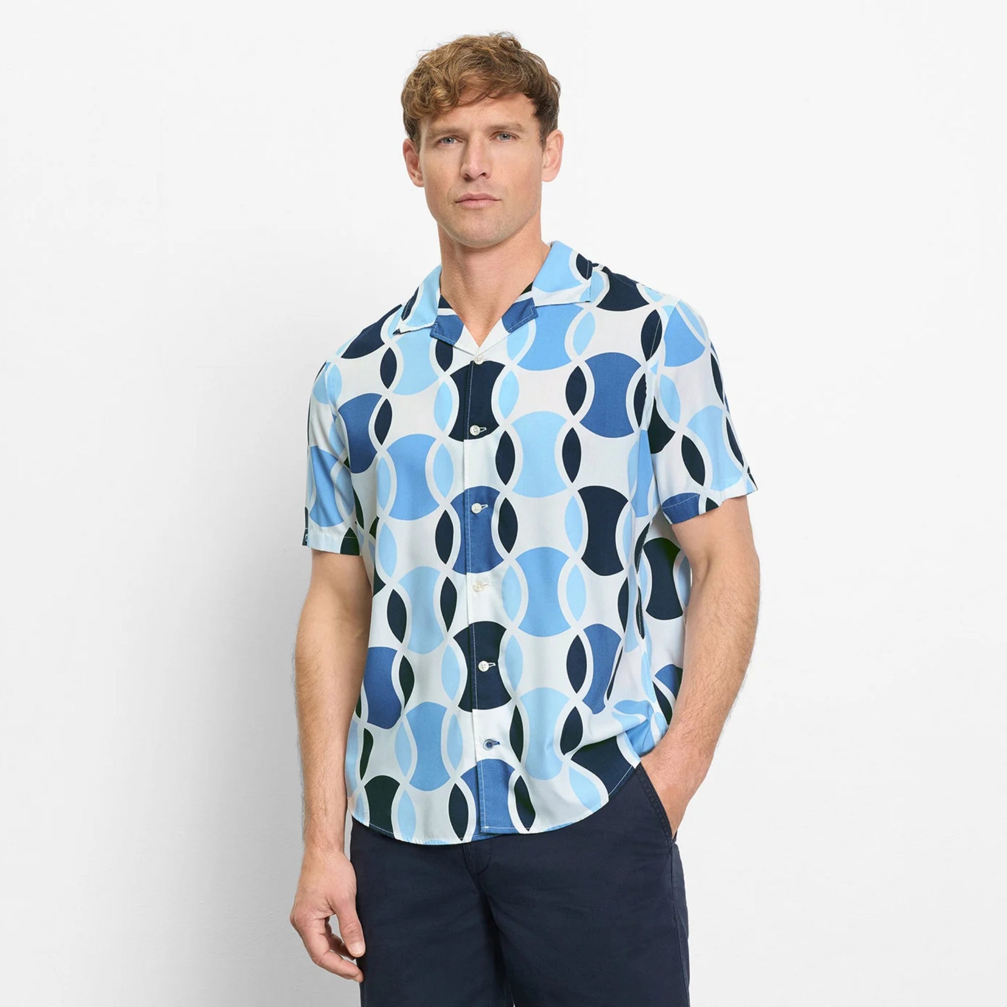 Man wearing a patterned shirt with blue and white design on a plain background