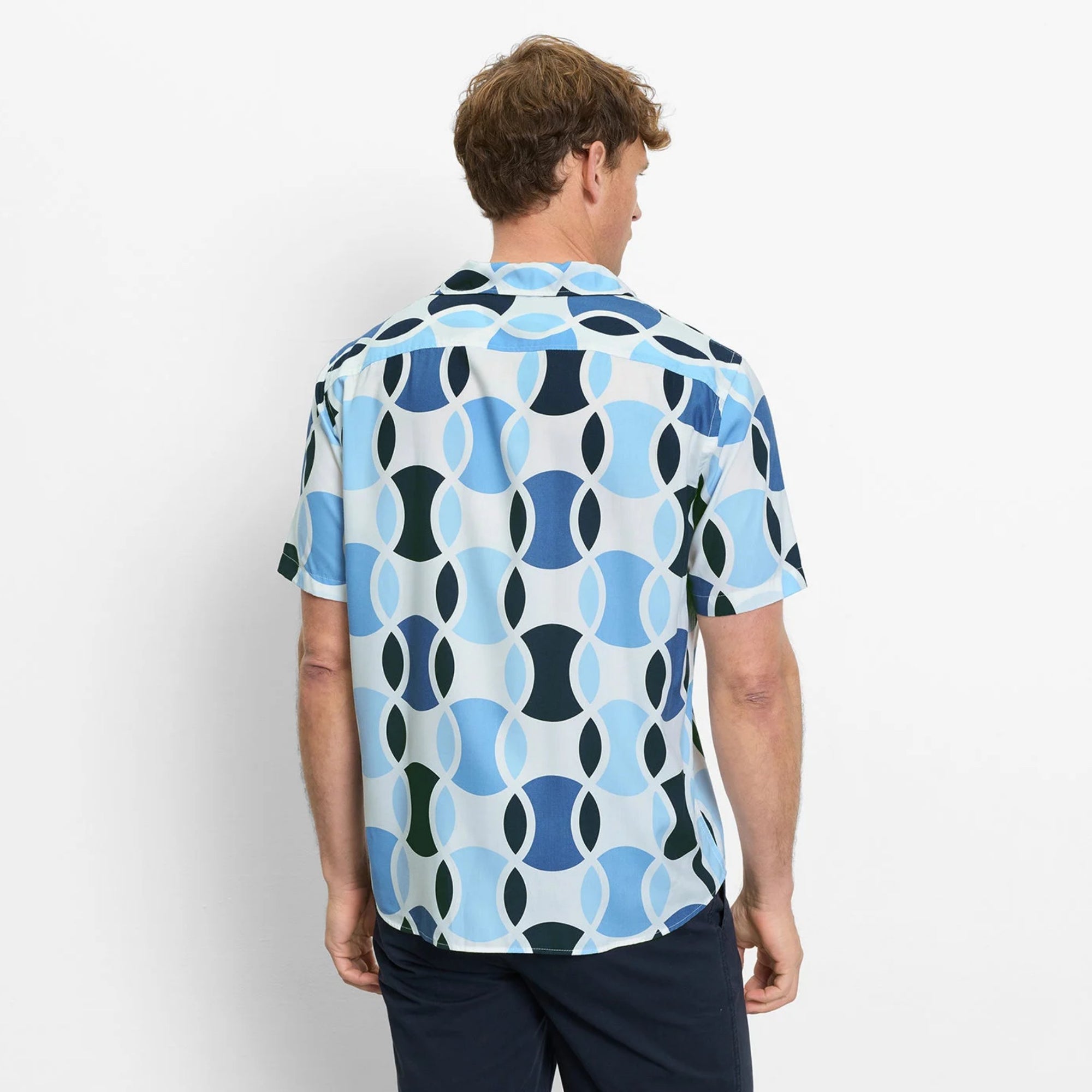 Man wearing a patterned shirt with blue and green geometric design on a white background