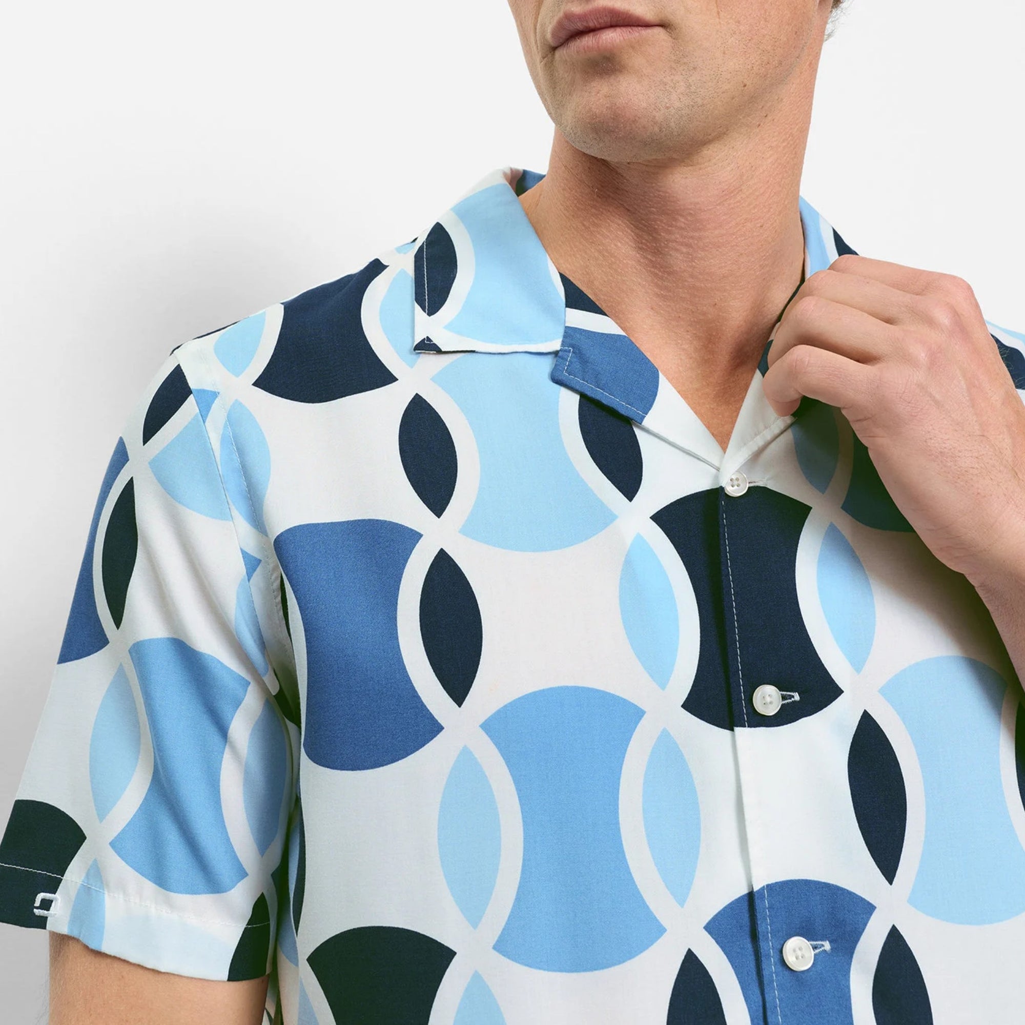Man wearing a patterned shirt with blue, white, and black design on a plain background