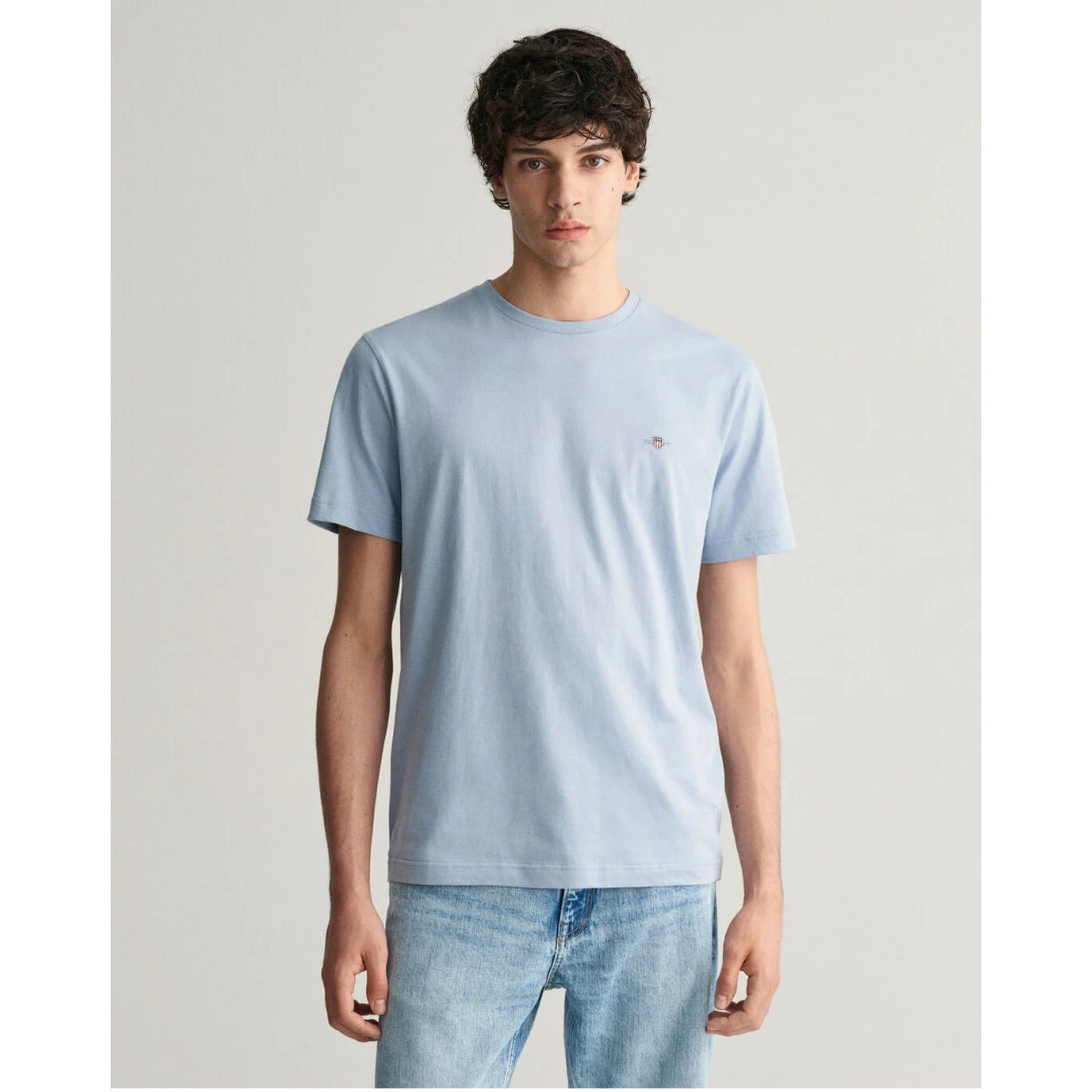 Man wearing a light blue t-shirt with a small logo on a plain background