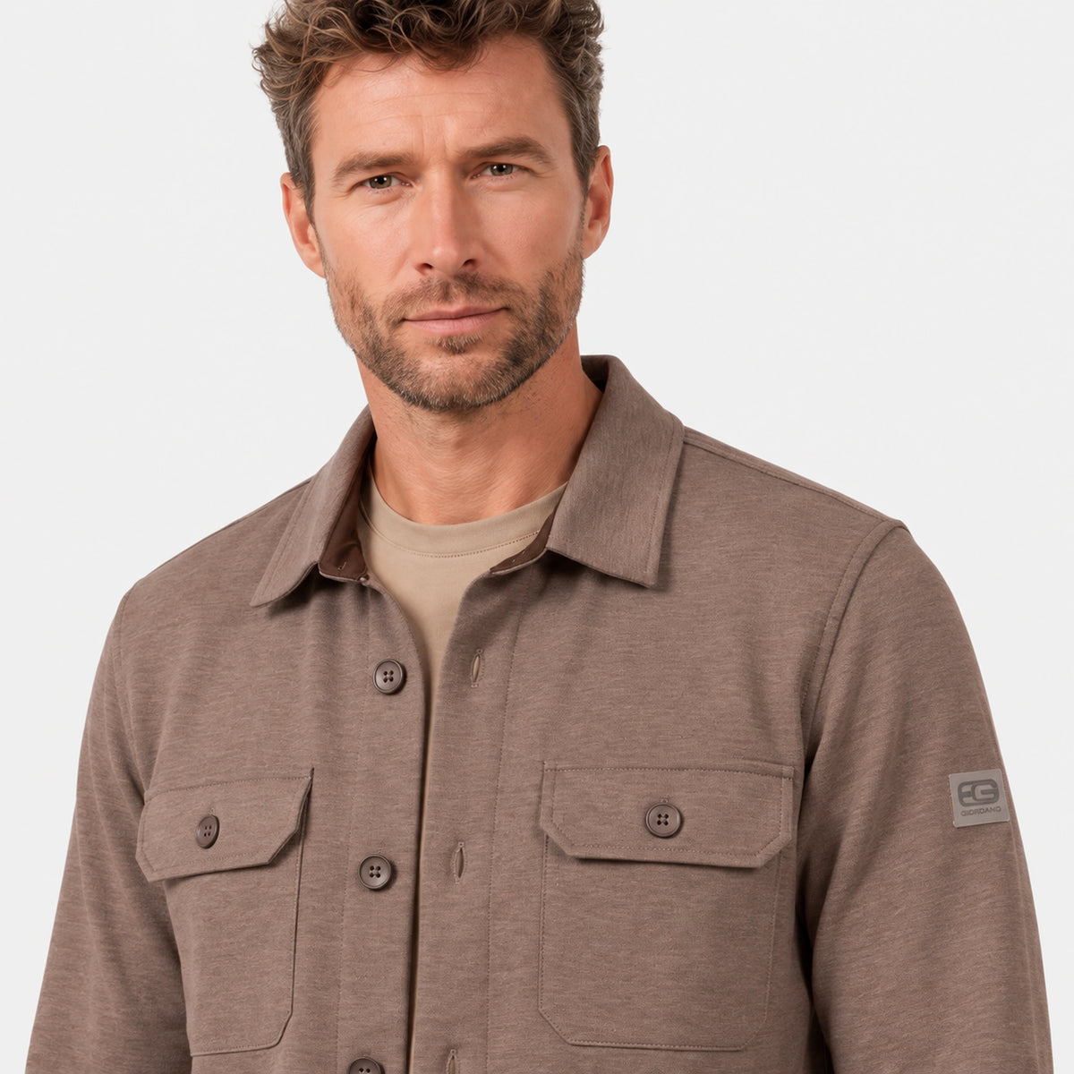 Close-up of the Giordano Taranto Shell beige overshirt, showing the jersey texture, collar, buttoned chest pockets and sleeve badge.