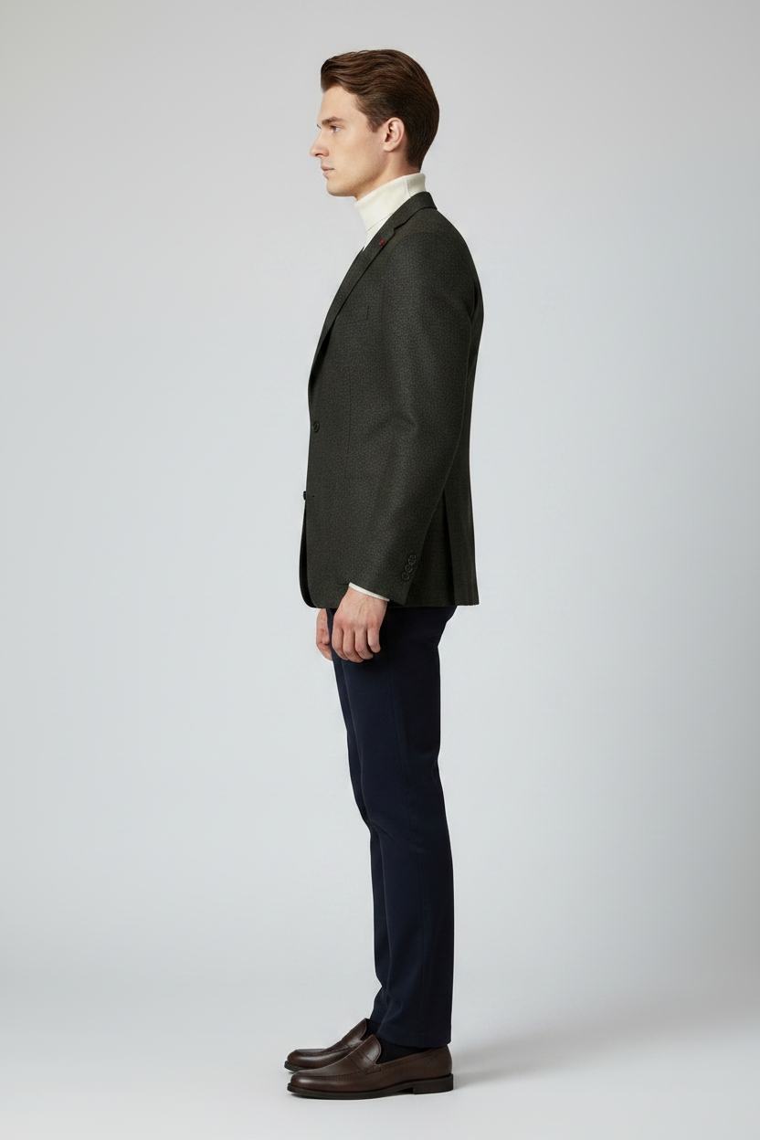 A man modeling a dark charcoal gray textured blazer over a cream turtleneck sweater, paired with navy blue trousers and dark brown dress shoes, against a light gray studio background.
