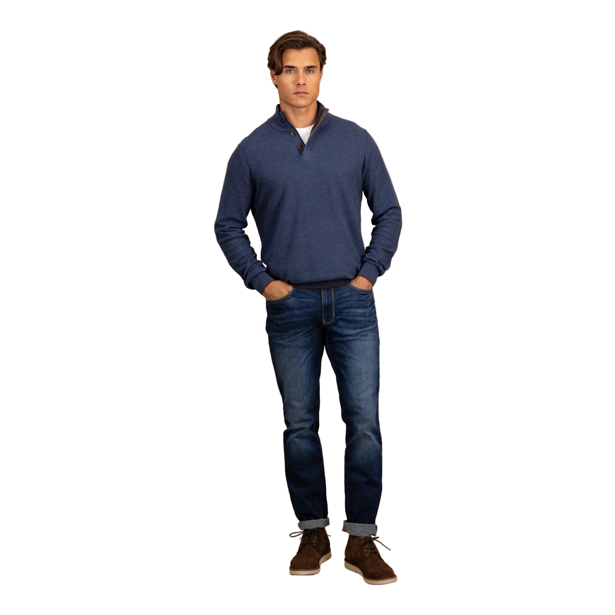 Man wearing a blue sweater and jeans standing against a beige background