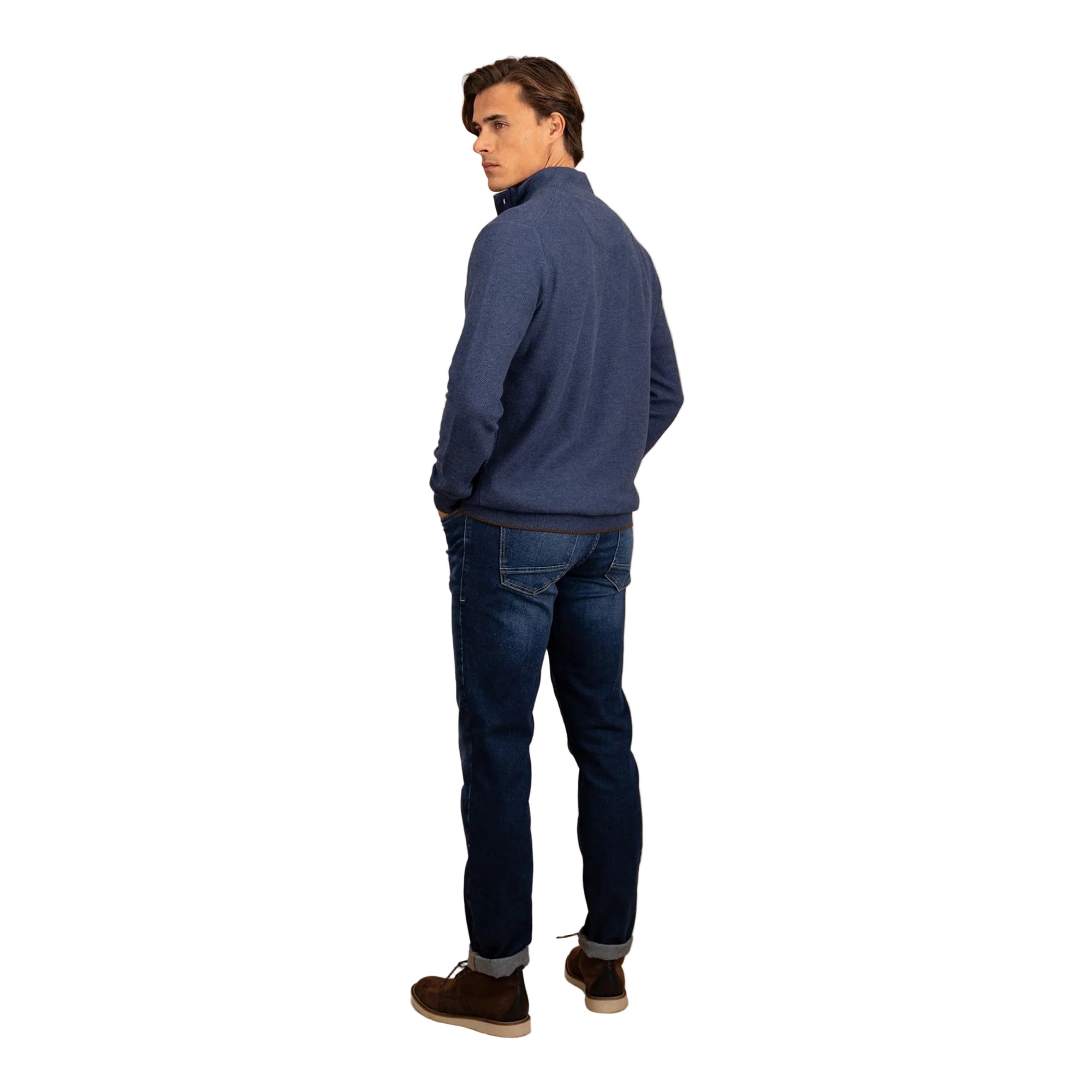 Man wearing a blue sweater and jeans standing against a beige background